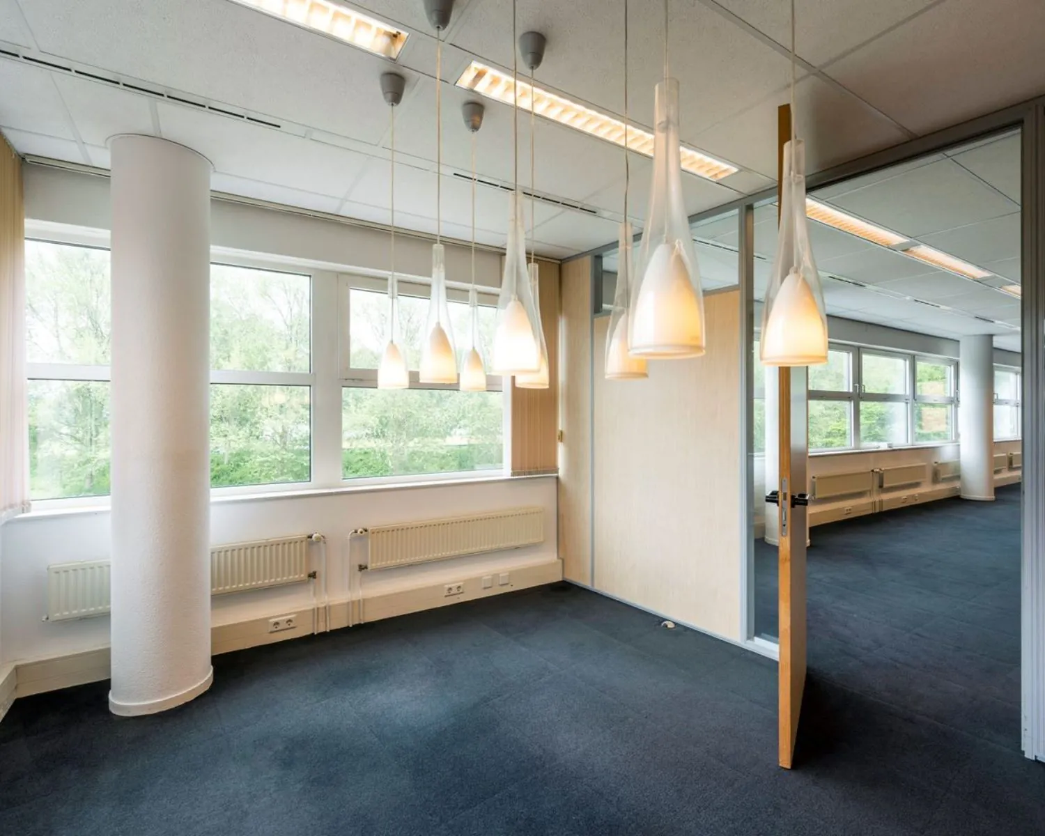 Moderne kantoorruimte in Entrada 300 te Amsterdam met grote ramen, donker tapijt en hanglampen.