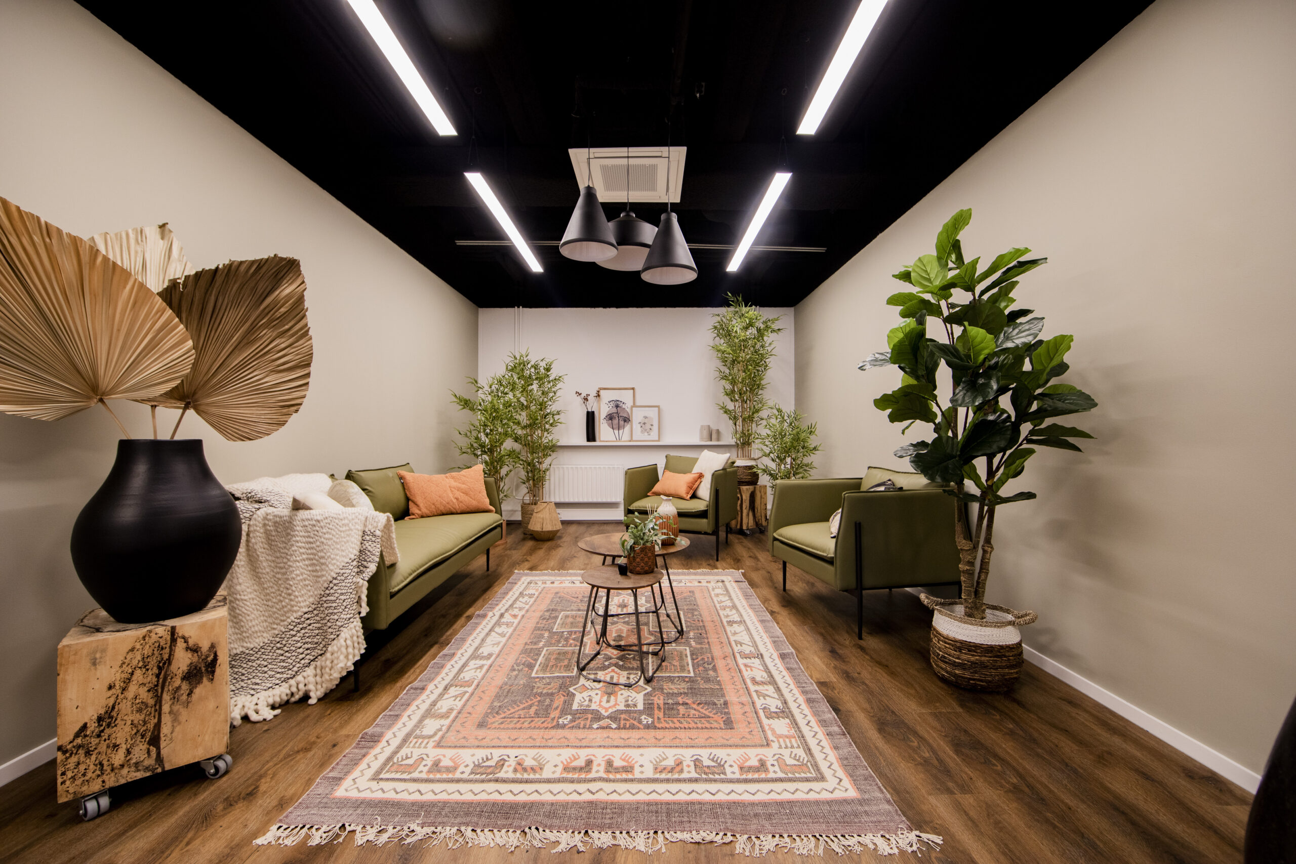 Stijlvolle kantoorruimte met planten, loungesofa's en een kleurrijk tapijt op de vloer.