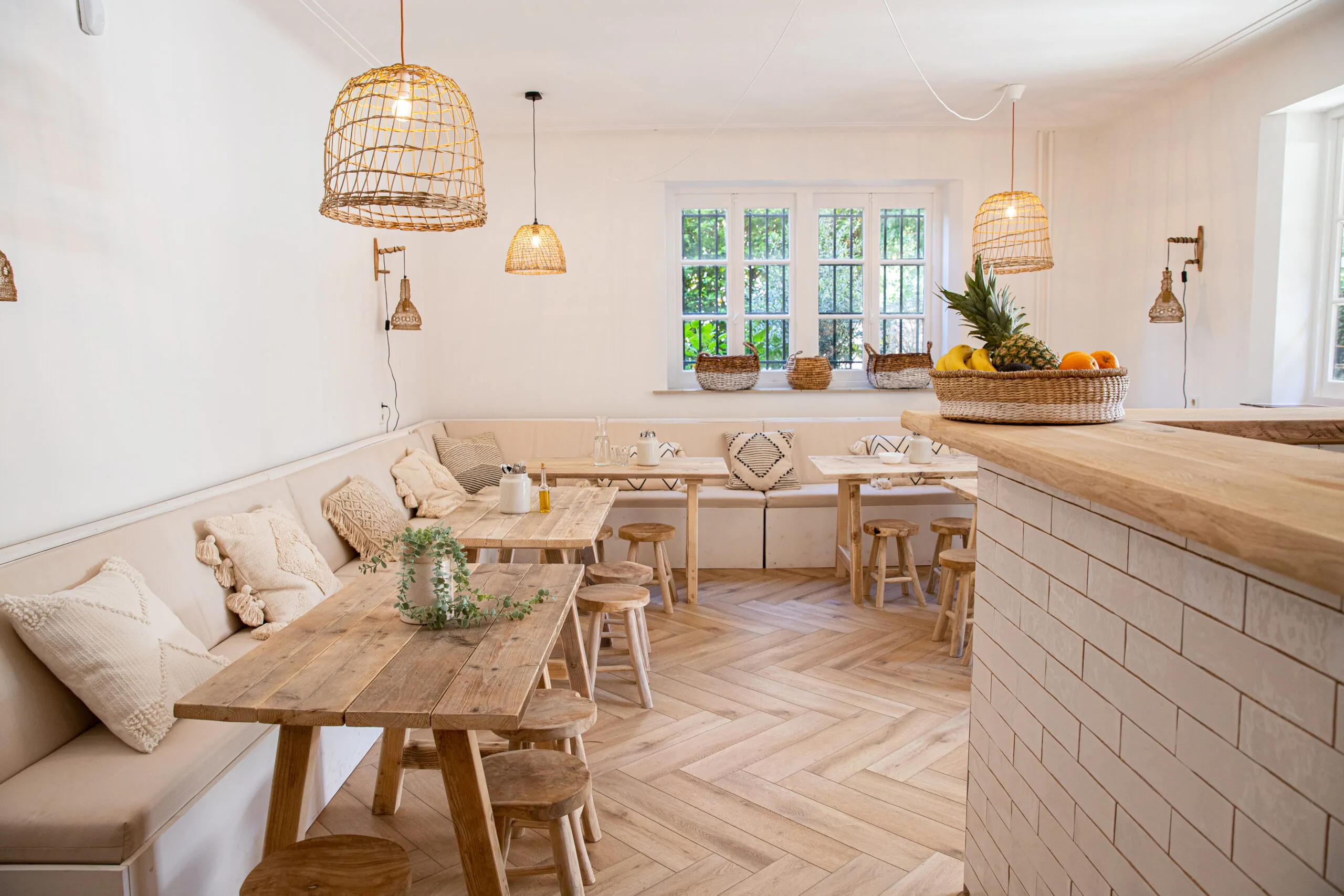Licht en sfeervol interieur van Creativegrounds – Emmalaan met houten meubels, rieten lampen en een fruitschaal op de bar.