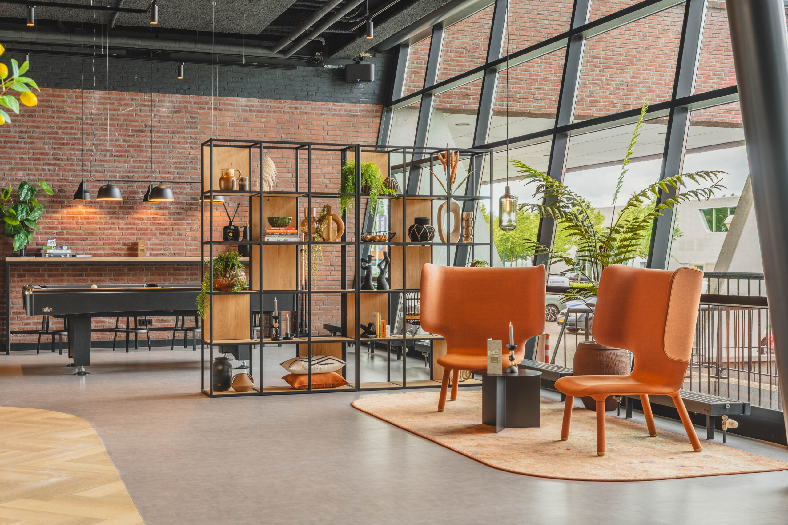 Een stijlvolle zitruimte bij Entree Rijnzathe met oranje fauteuils, een decoratieve kast en grote ramen die veel licht binnenlaten.