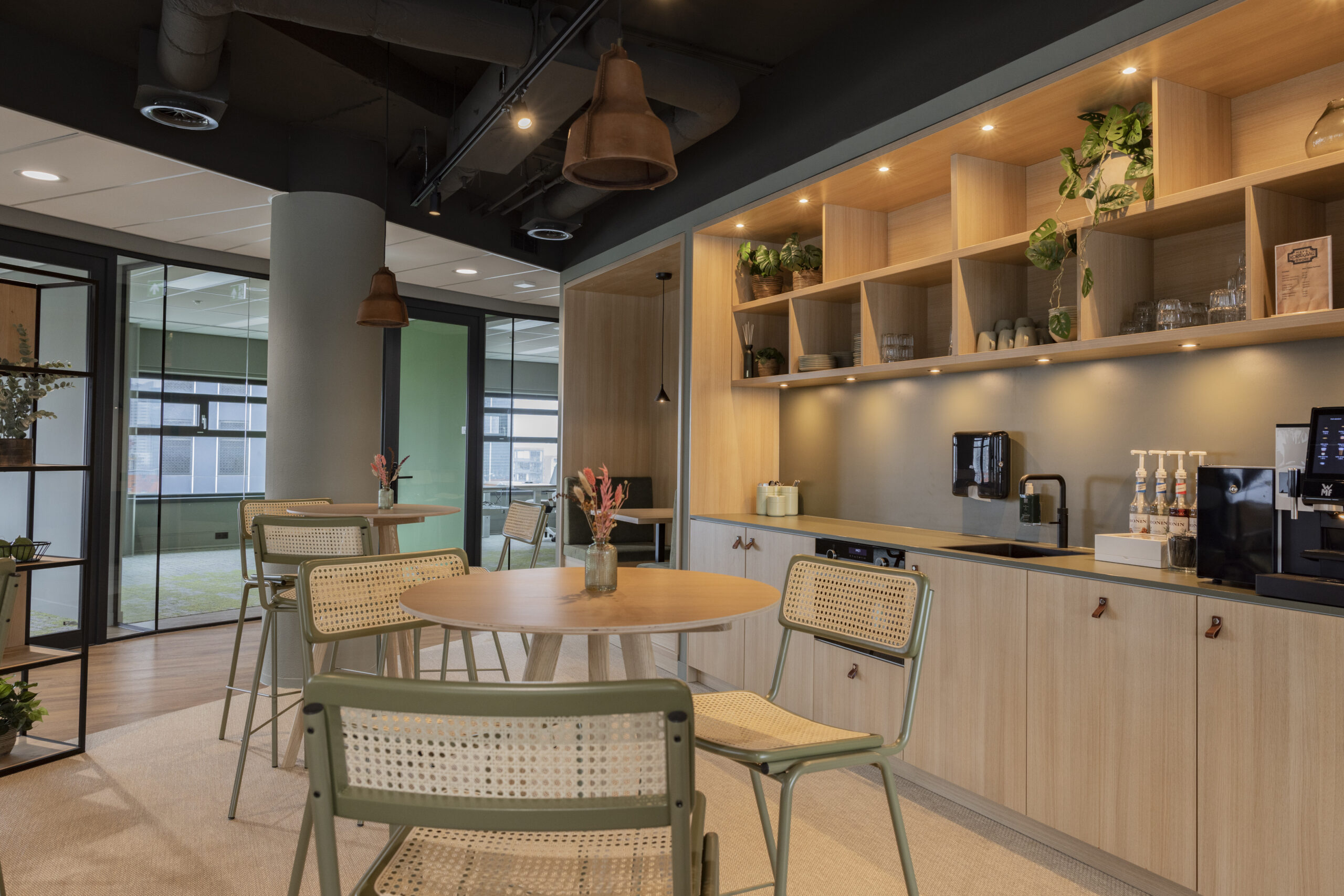 Moderne kantoorruimte met houten meubels, planten en een koffiehoek in een open ruimte.