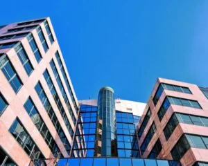 Vooraanzicht van een modern kantoorgebouw met glazen gevel en roze stenen elementen tegen een blauwe lucht.