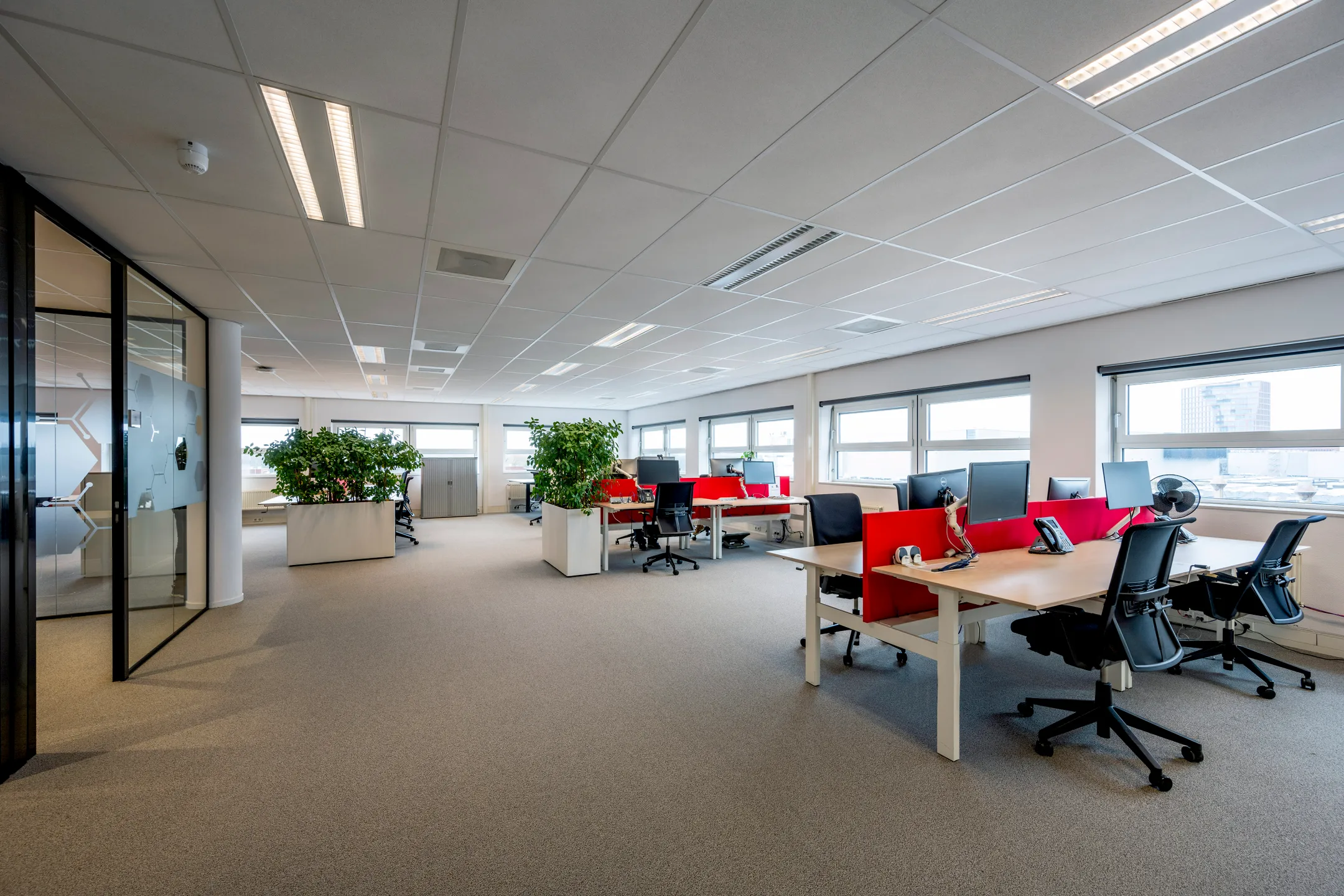 Een modern en ruim kantoor met bureaus, stoelen en grote ramen die uitzicht bieden.