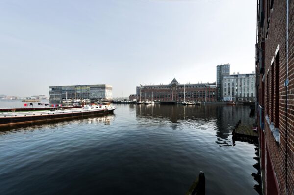 Uitzicht op het water van de Van Diemenstraat in Amsterdam met boten en moderne en historische gebouwen aan de kade.