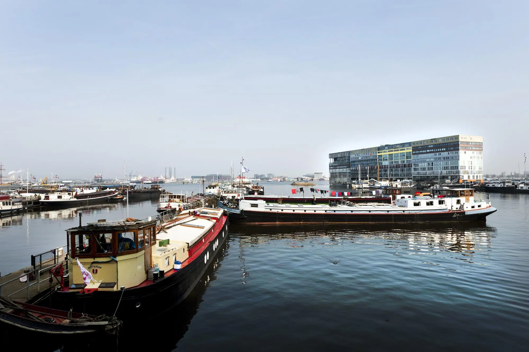 Uitzicht op de Van Diemenstraat in Amsterdam met aangemeerde woonboten en een modern kantoorgebouw aan het water.