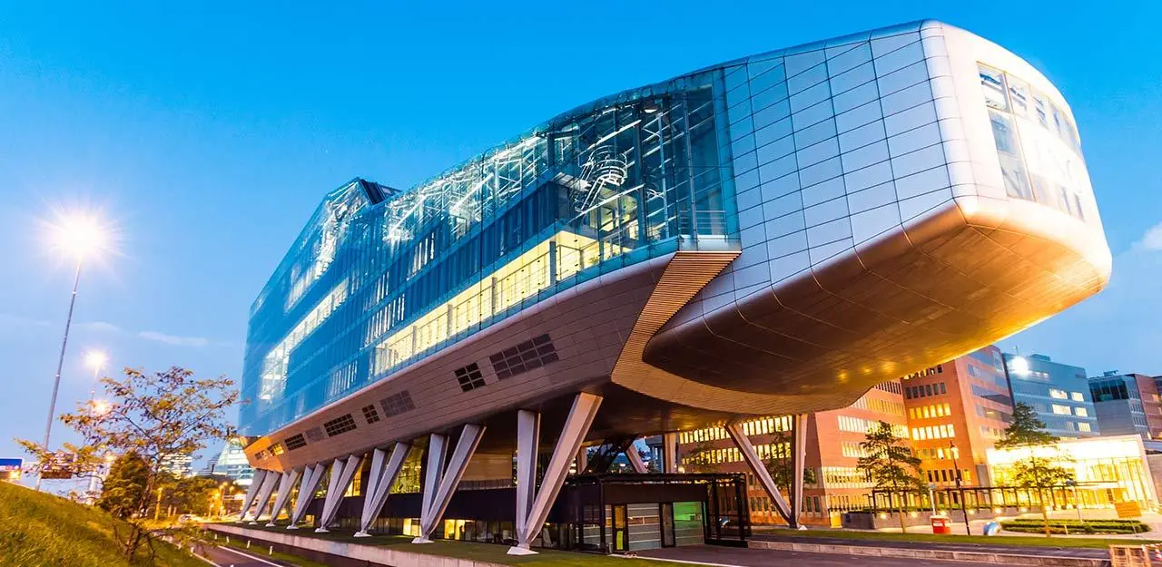 Modern kantoorgebouw aan de Amstelveenseweg in Amsterdam met futuristisch design en glazen gevel, gefotografeerd tijdens zonsondergang.