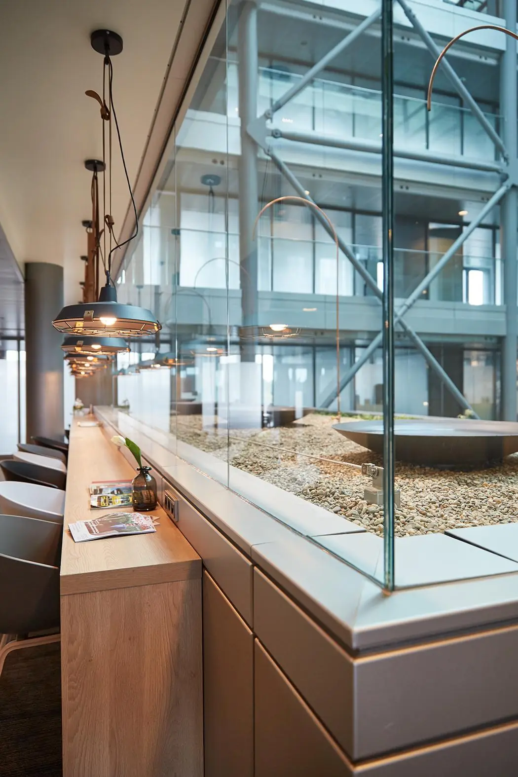 Moderne wachtruimte aan de Amstelveenseweg met houten blad, hanglampen en zicht op een glazen binnentuin met grind.