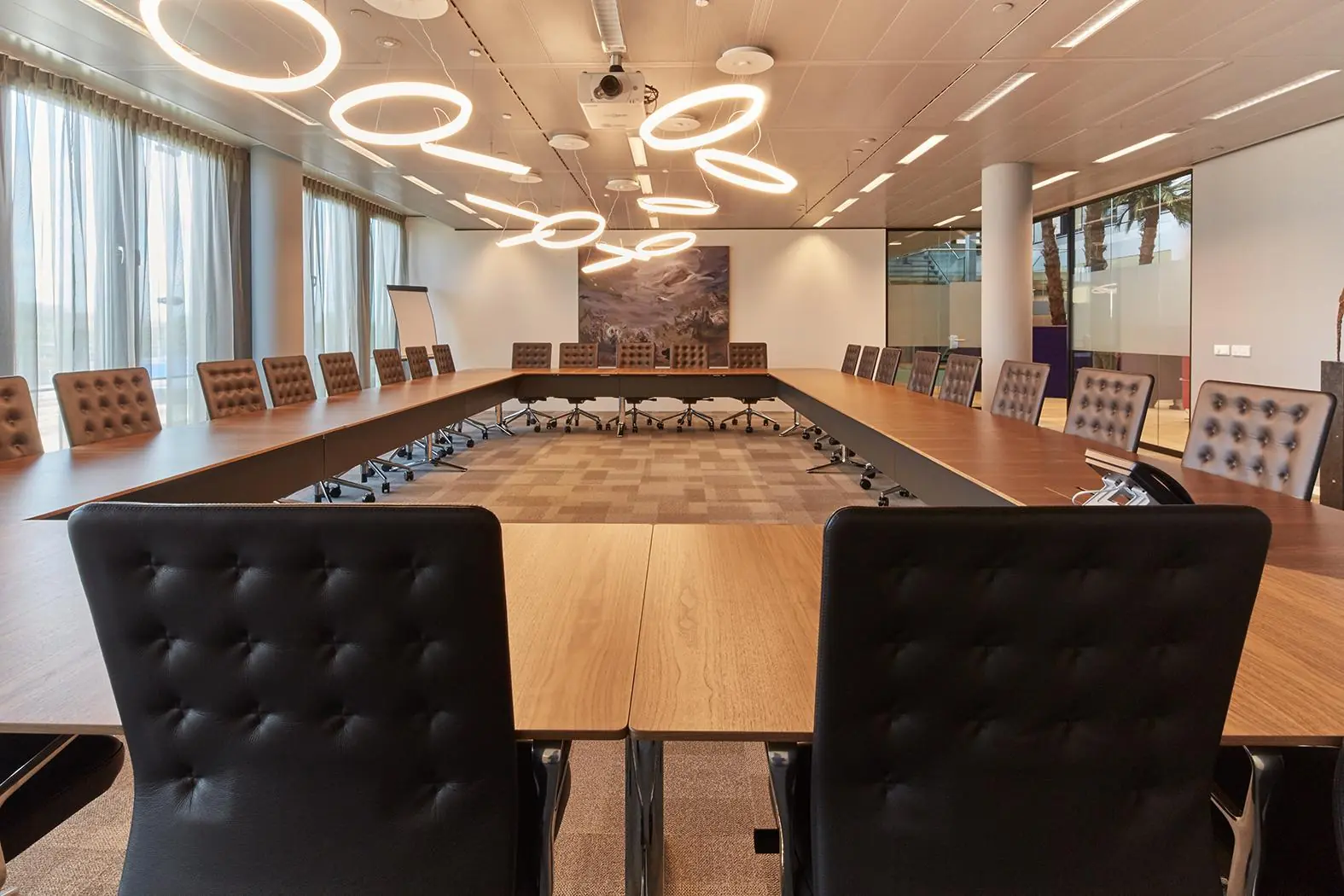 Moderne vergaderruimte aan de Amstelveenseweg met een U-vormige tafel, leren stoelen en futuristische ringlampen.