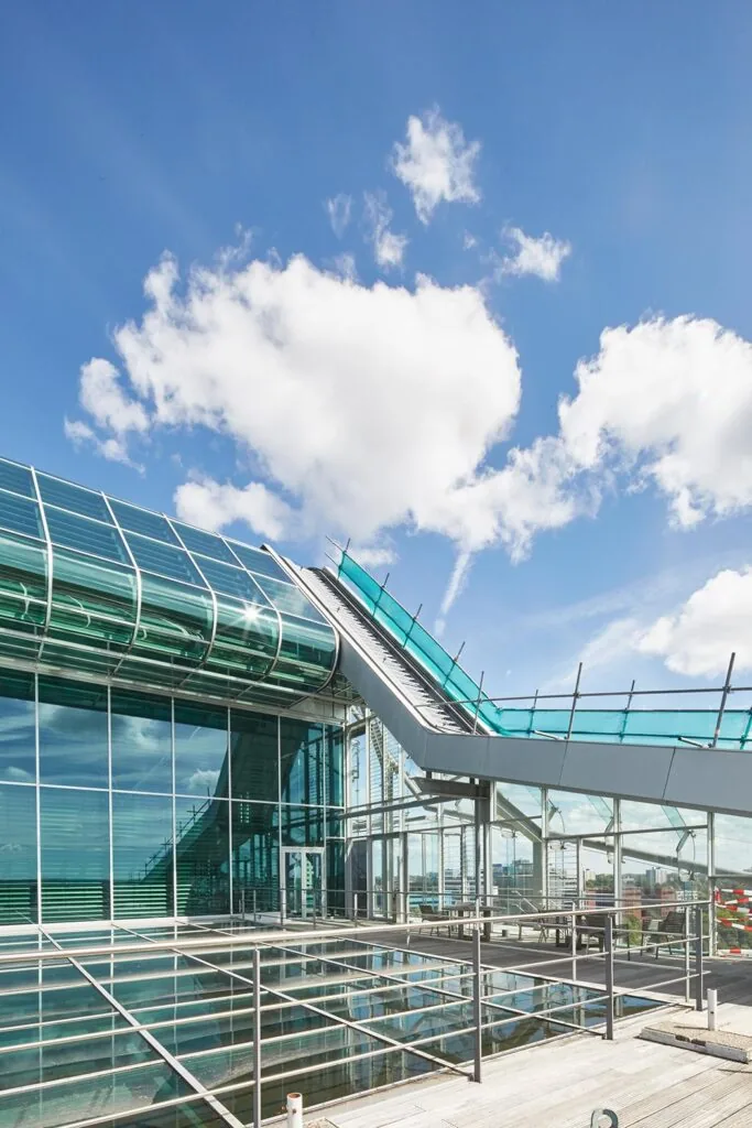 Modern glazen kantoorgebouw aan de Amstelveenseweg met een opvallend schuindak en blauwe lucht op de achtergrond.