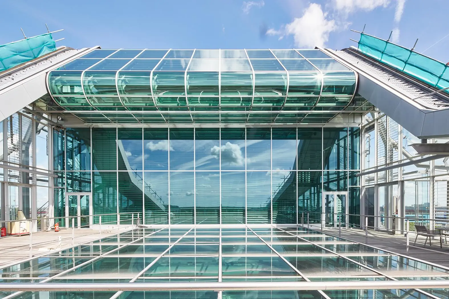 Moderne glazen gevel en glazen loopbrug van een gebouw aan de Amstelveenseweg, weerspiegelend in het glazen oppervlak.