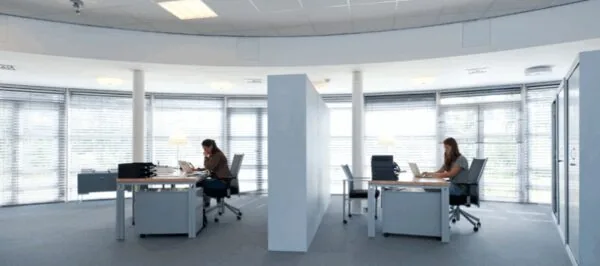Twee personen werken op laptops in een modern, licht kantoor aan de Arlandaweg met grote ramen en glazen tussenwanden.