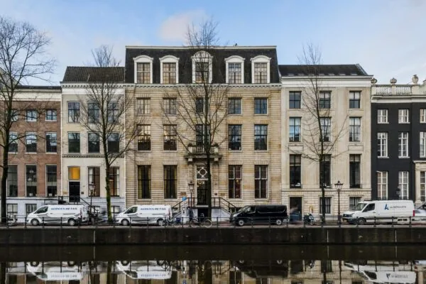 Monumentaal grachtenpand aan de Herengracht in Amsterdam, met geparkeerde bestelbusjes en kale bomen langs het water.