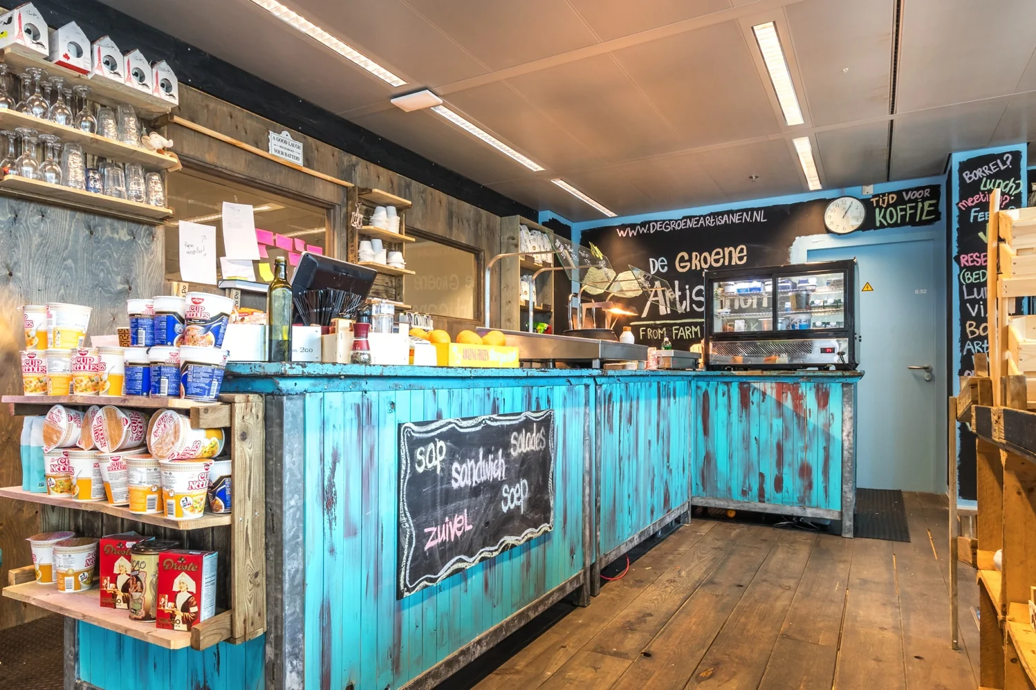 Kleurrijke lunchcounter van De Groene Artisanen aan de Reactorweg met houten inrichting en diverse snacks en dranken.