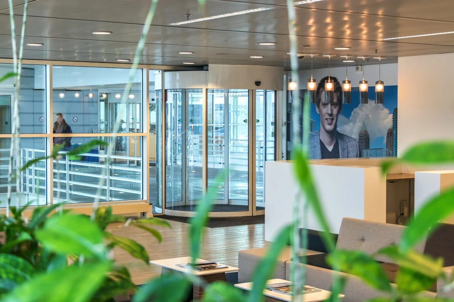 Moderne kantoorentree aan de Reactorweg met glazen draaideur, wachtruimte en muurdecoratie van een man en stadspand.