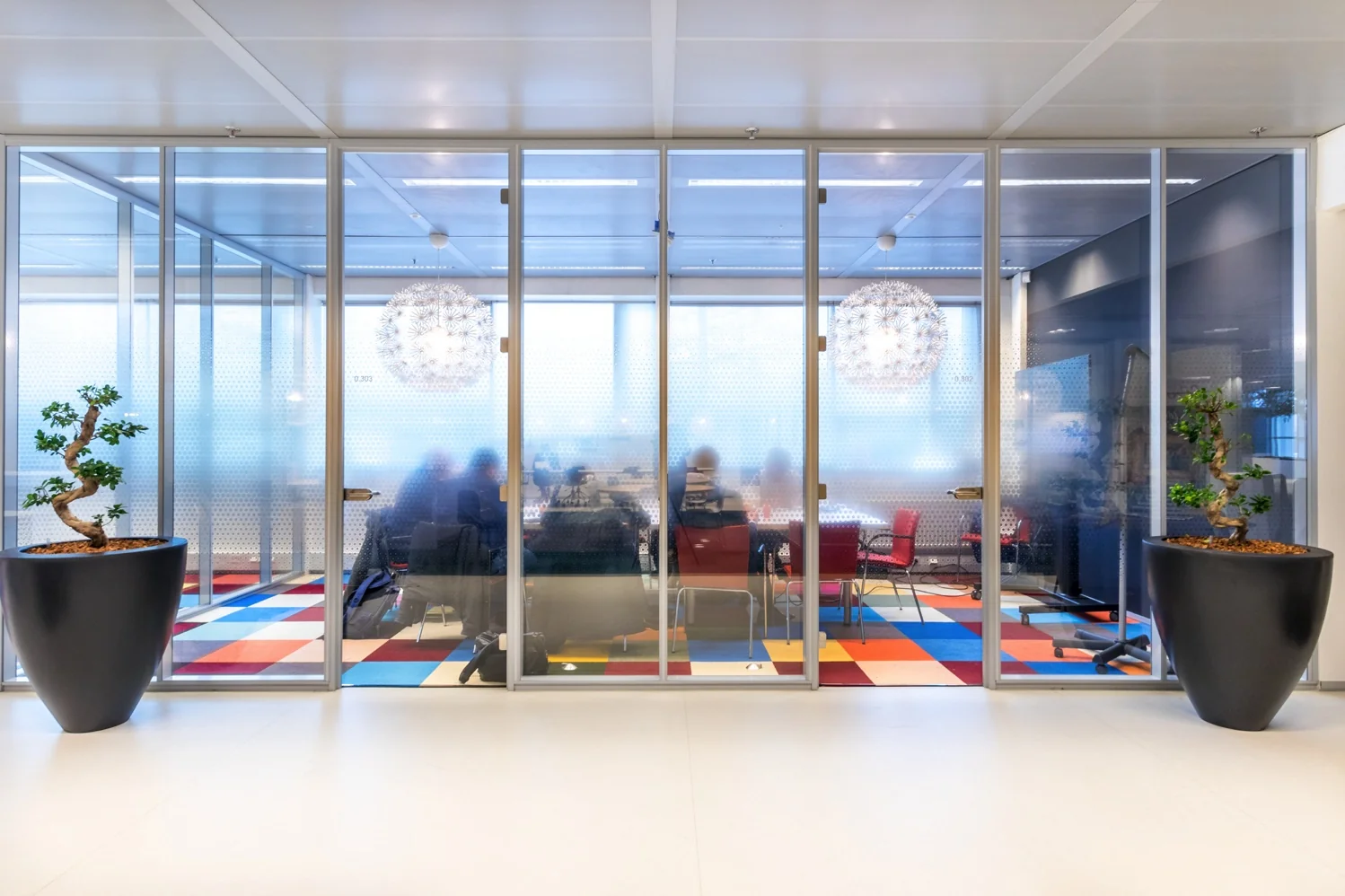 Vergaderruimte aan de Reactorweg met glazen wanden, kleurrijk vloer tapijt en zichtbare silhouetten van mensen in overleg.