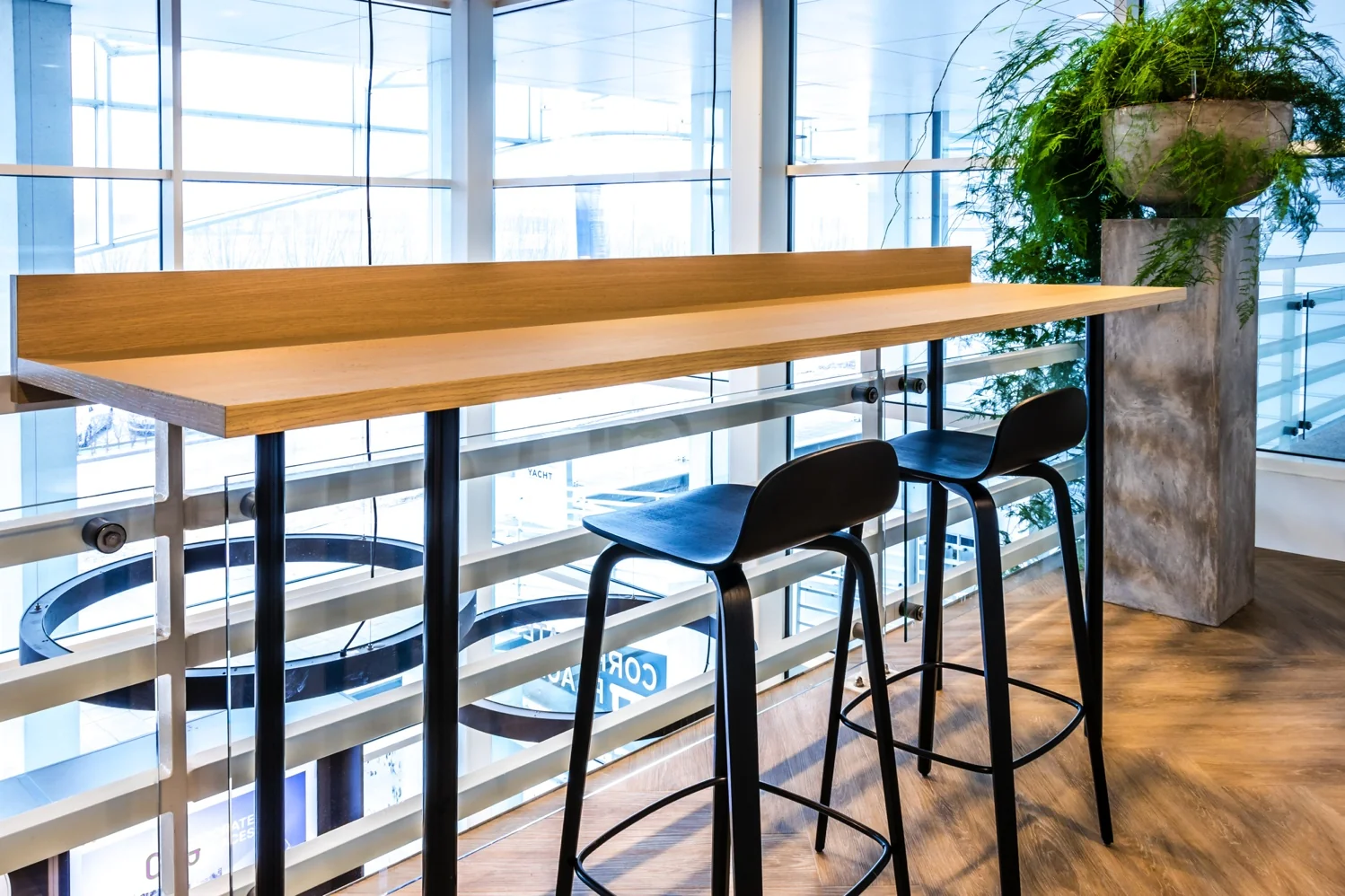 Hoge zitplek met houten bartafel, twee zwarte barkrukken en een grote plantenbak in een modern kantoorgebouw aan de Reactorweg.