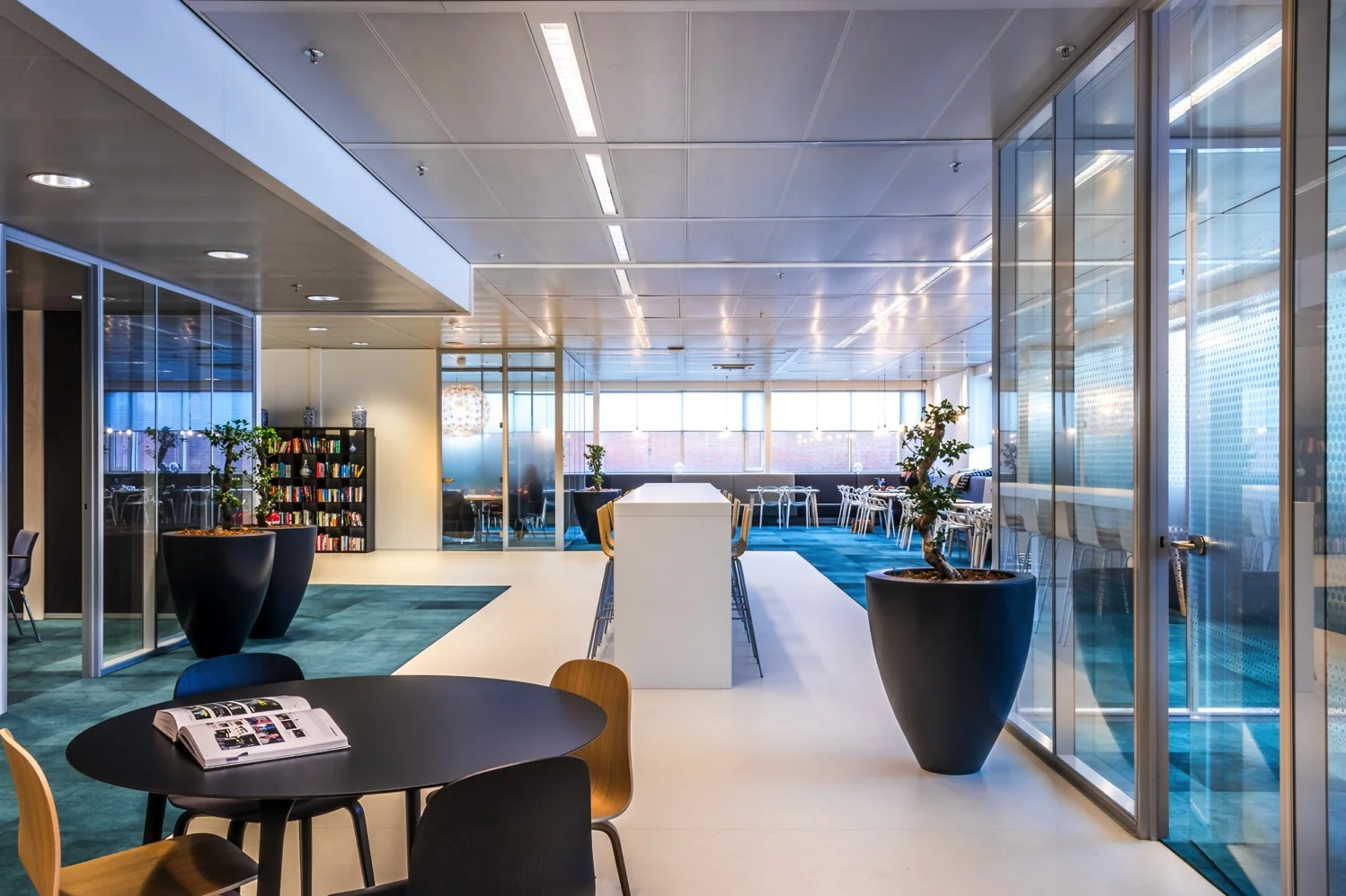Modern ingerichte kantoorruimte aan de Reactorweg met glazen vergaderruimtes, een centrale leestafel en veel daglicht.