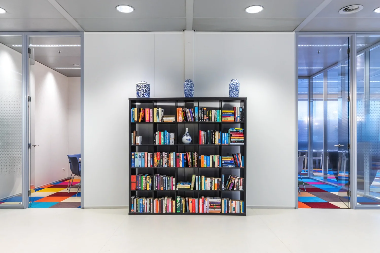 Boekenkast met diverse boeken en blauwe porseleinen vazen in een moderne kantoorruimte aan de Reactorweg.