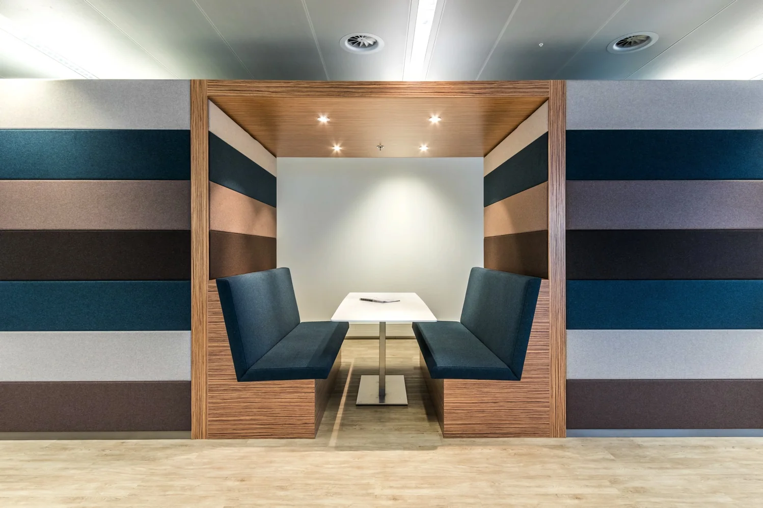 Moderne zitnis met twee blauwe banken en een witte tafel, ingebouwd in een wand met horizontale gekleurde panelen aan de Reactorweg.