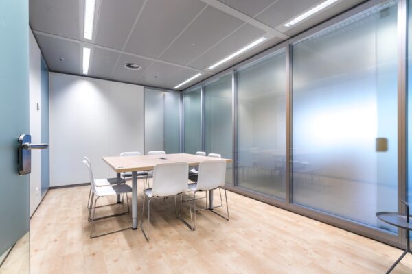 Vergaderruimte aan de Reactorweg met glazen wanden, houten vloer en witte stoelen rond een tafel.