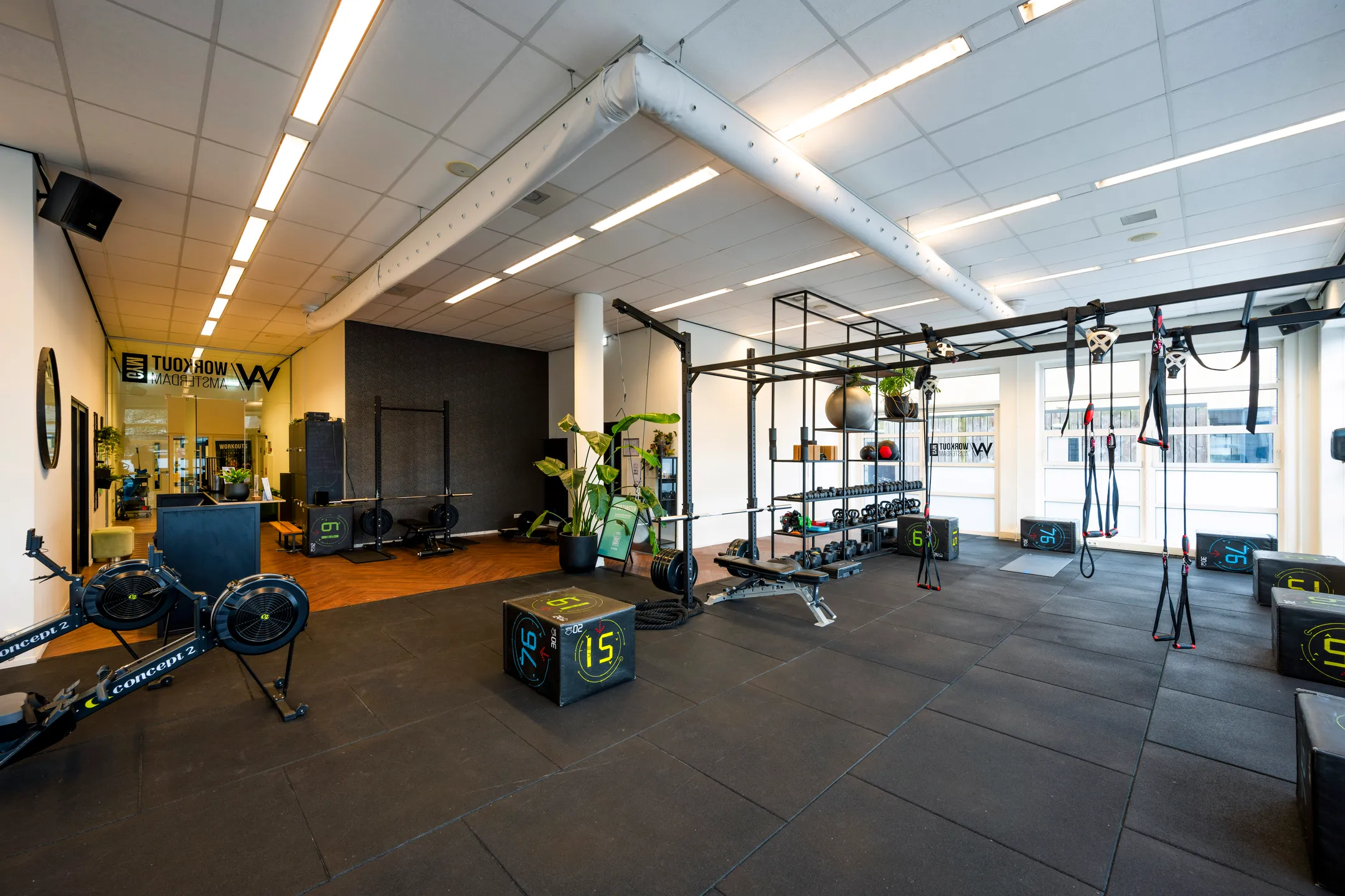Een moderne fitnessruimte met verschillende trainingsapparaten en een hoog plafond.