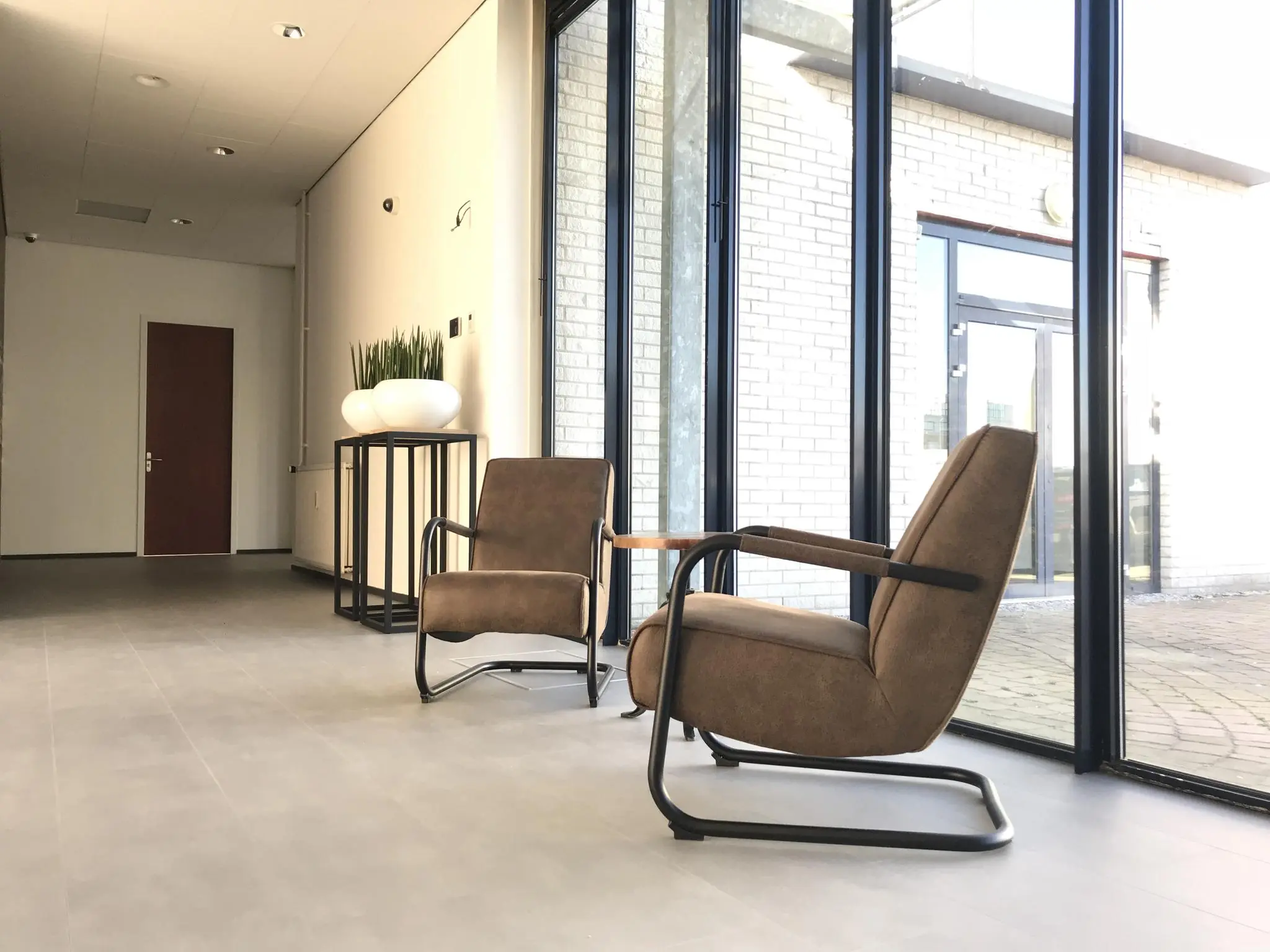 Moderne wachtruimte met twee bruine fauteuils bij een glazen gevel aan de Cypresbaan.