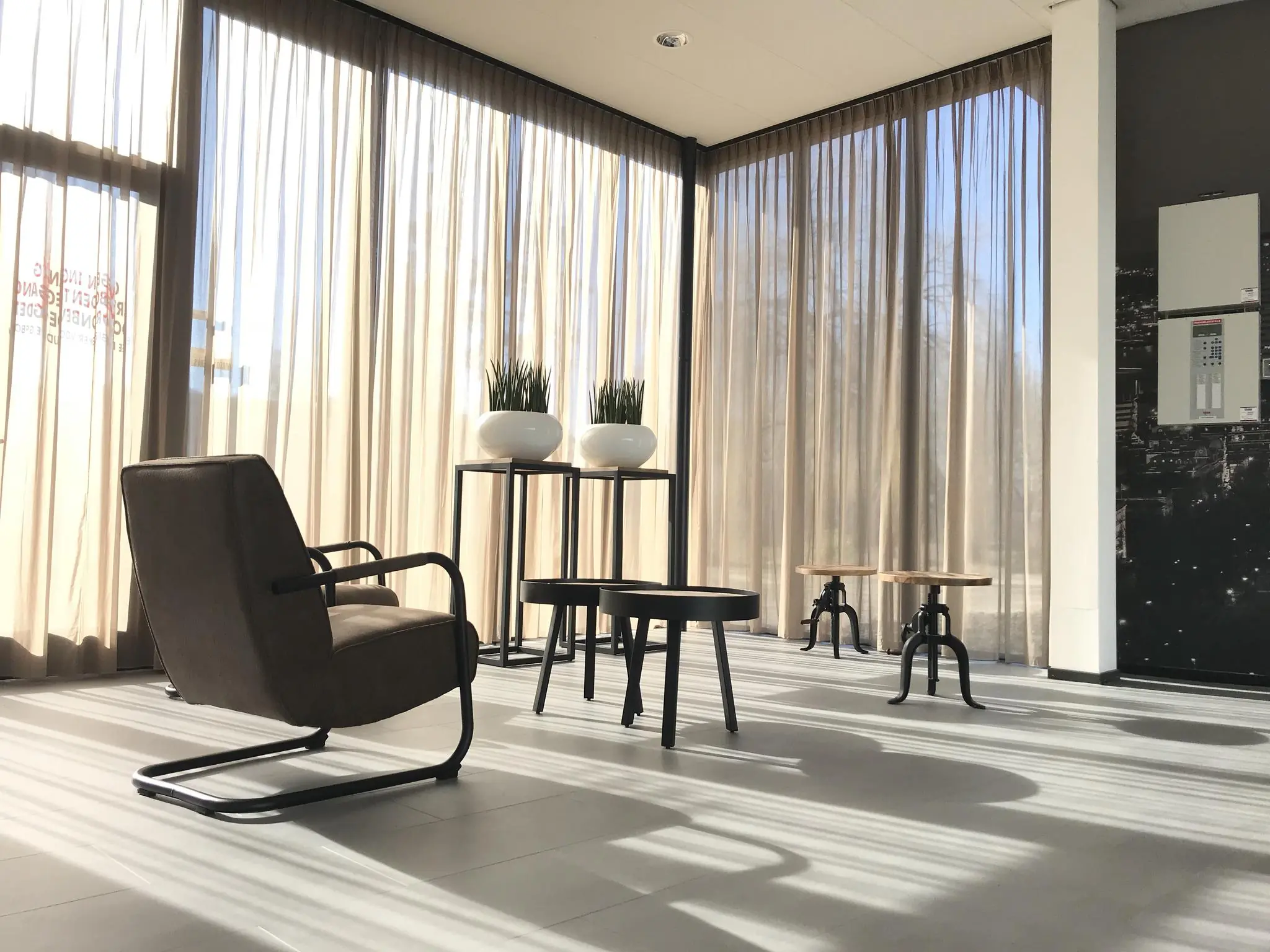 Moderne, zonovergoten wachtruimte met designmeubilair en grote ramen met lichte gordijnen aan de Cypresbaan.