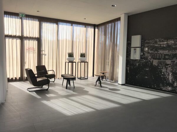 Lichte, moderne wachtruimte met stoelen, planten en een grote stadsfoto op de muur aan de Cypresbaan.
