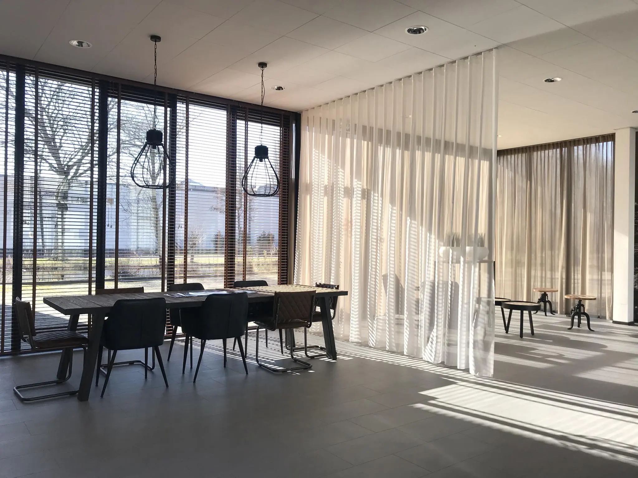 Moderne, lichte vergaderruimte aan de Cypresbaan met grote ramen, houten jaloezieën en een transparant gordijn als ruimteverdeler.