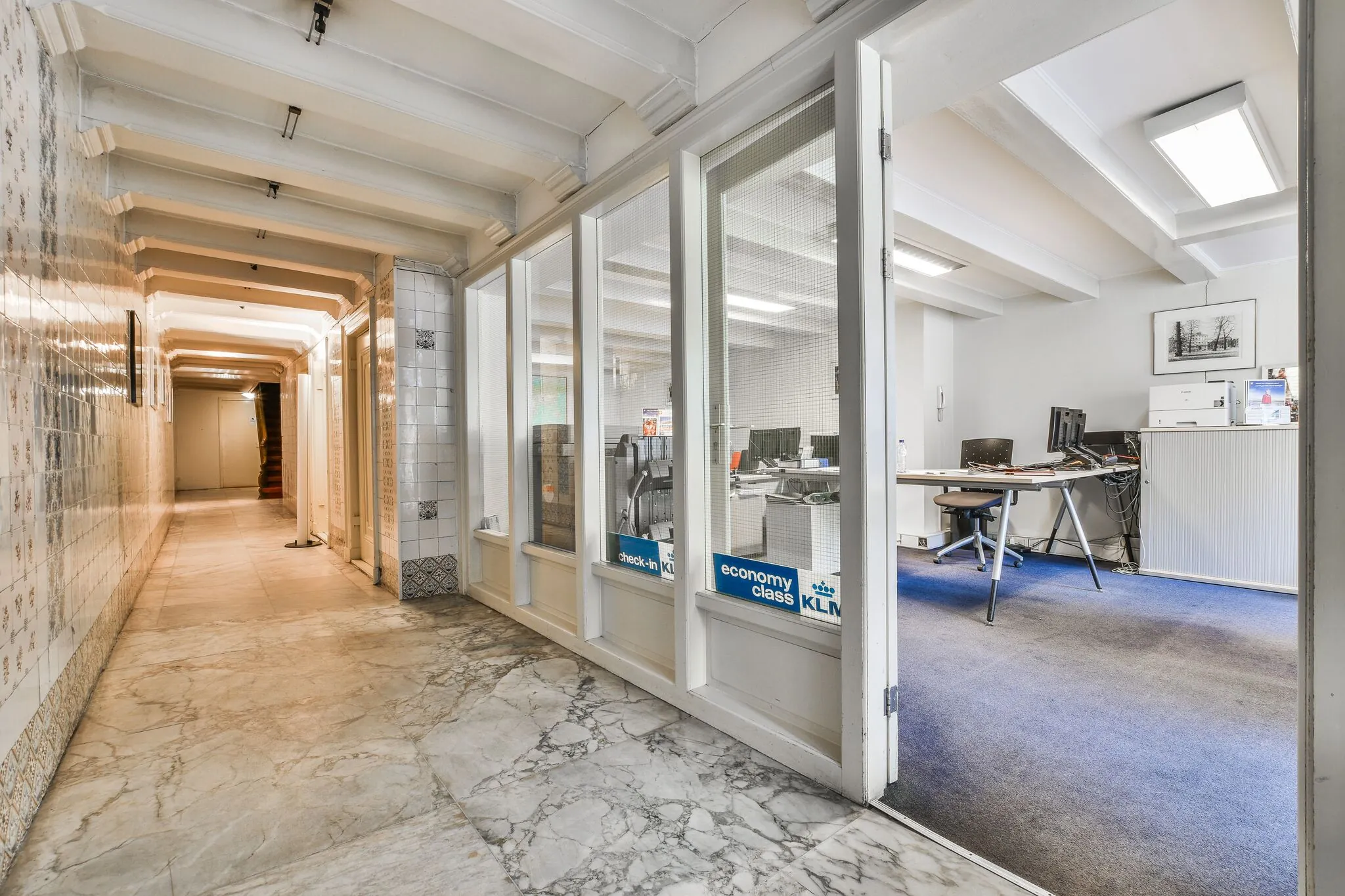 Hal met marmeren vloer en betegelde muren, met zicht op een kantoorruimte aan de Herengracht.