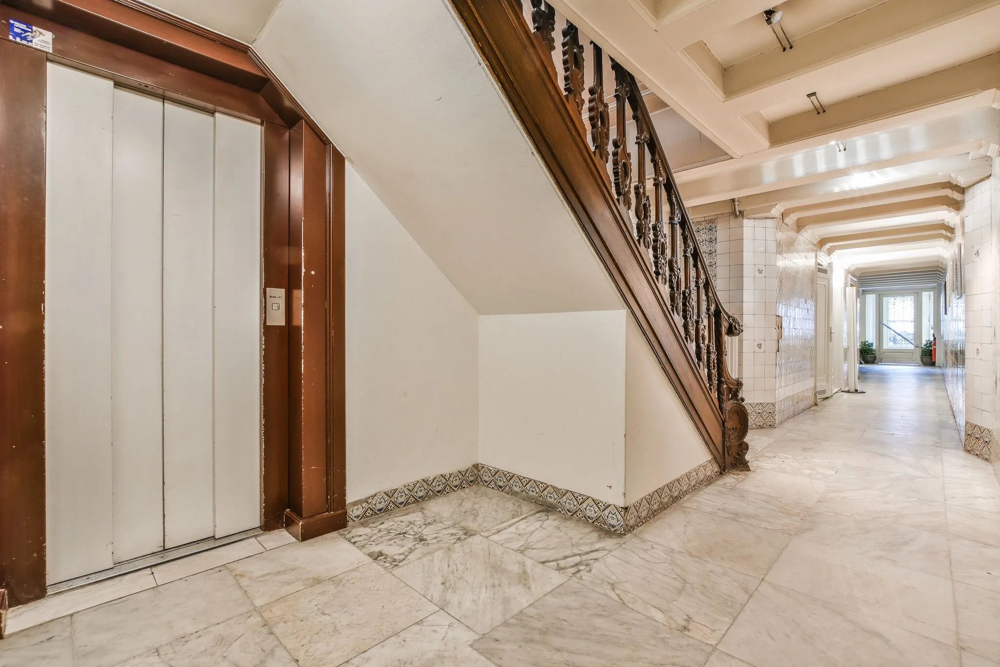 Marmeren gang in een klassiek grachtenpand aan de Herengracht met houten trapleuning en lift.