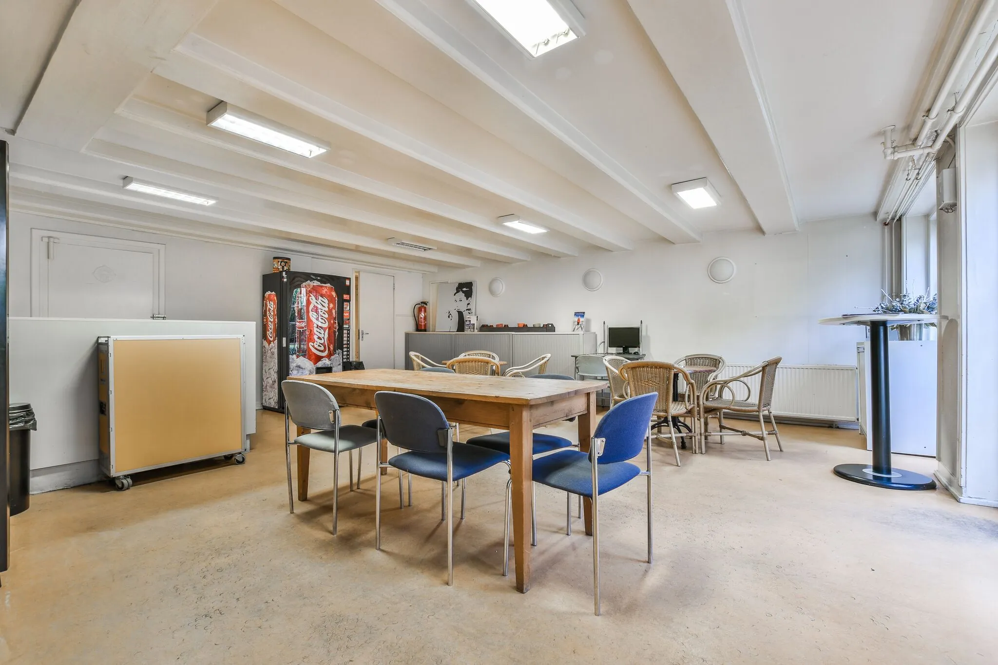 Kantineruimte aan de Herengracht met houten tafel, verschillende stoelen, een Coca-Cola automaat en een werkplek met computer.