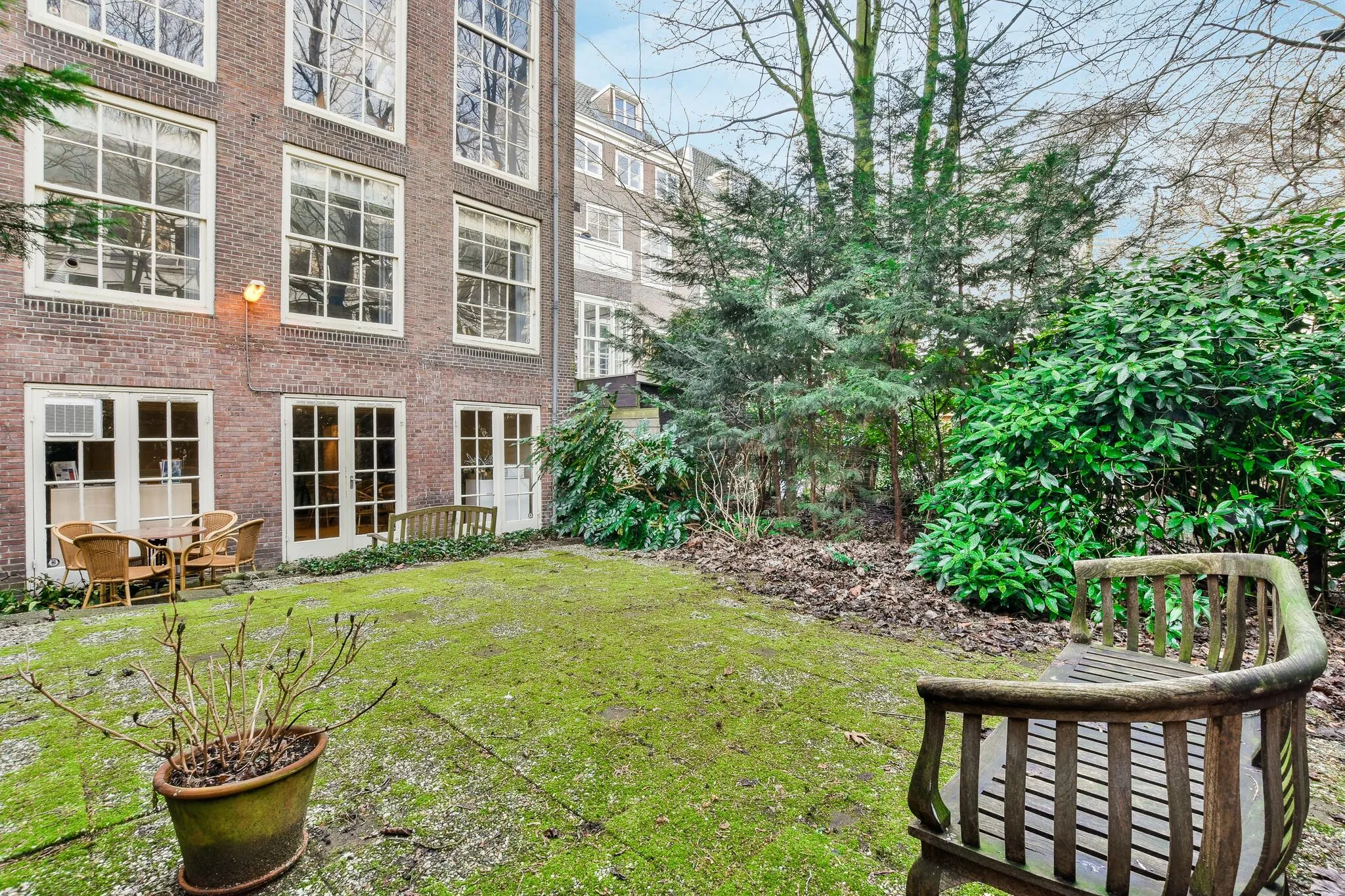 Binnenplaats met houten zitbank, mosgroene tegels en uitzicht op het achtergevel van een grachtenpand aan de Herengracht.