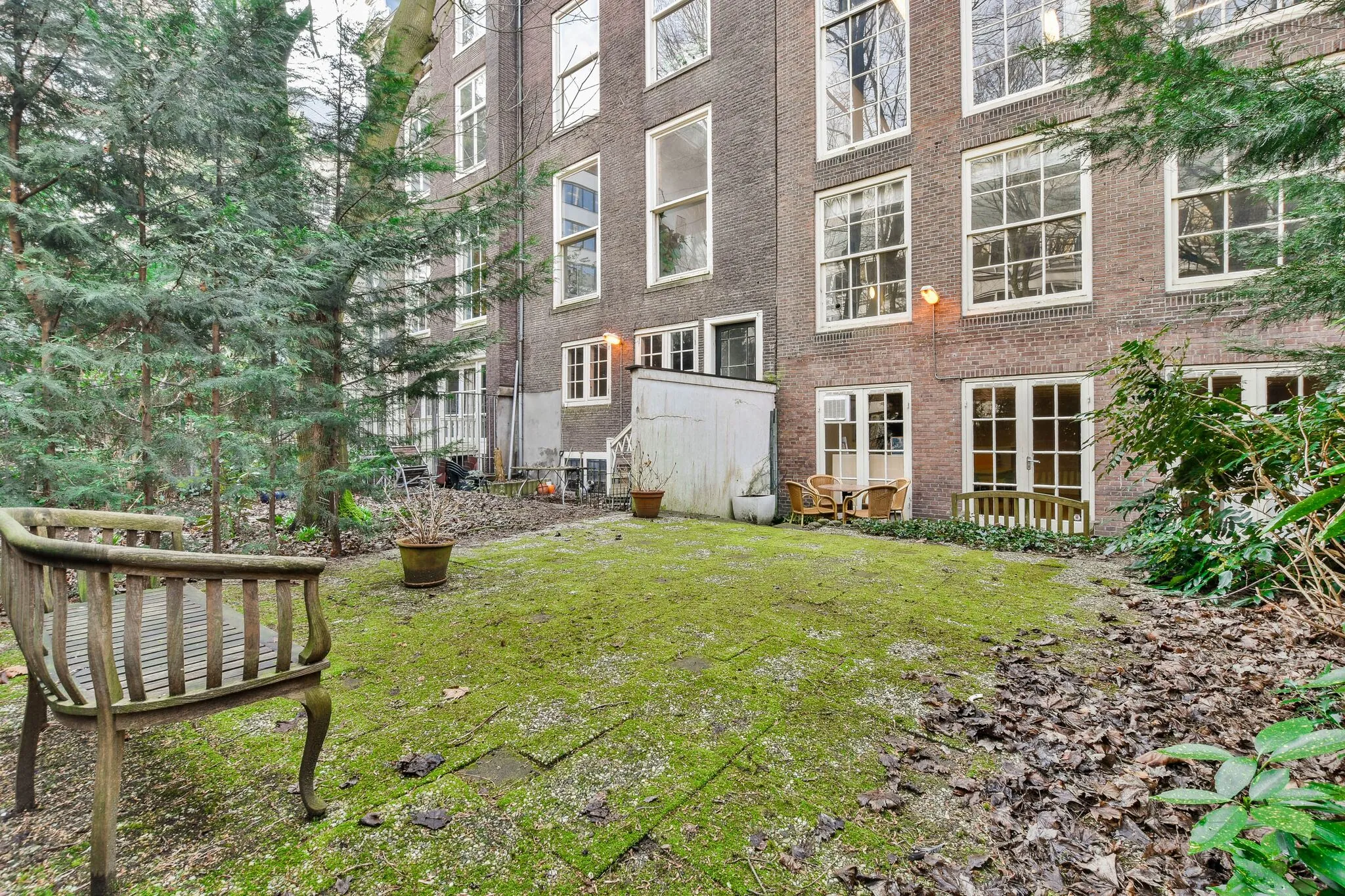 Achtertuin met mosbegroeiing, omringd door groen en grenzend aan een bakstenen pand aan de Herengracht.