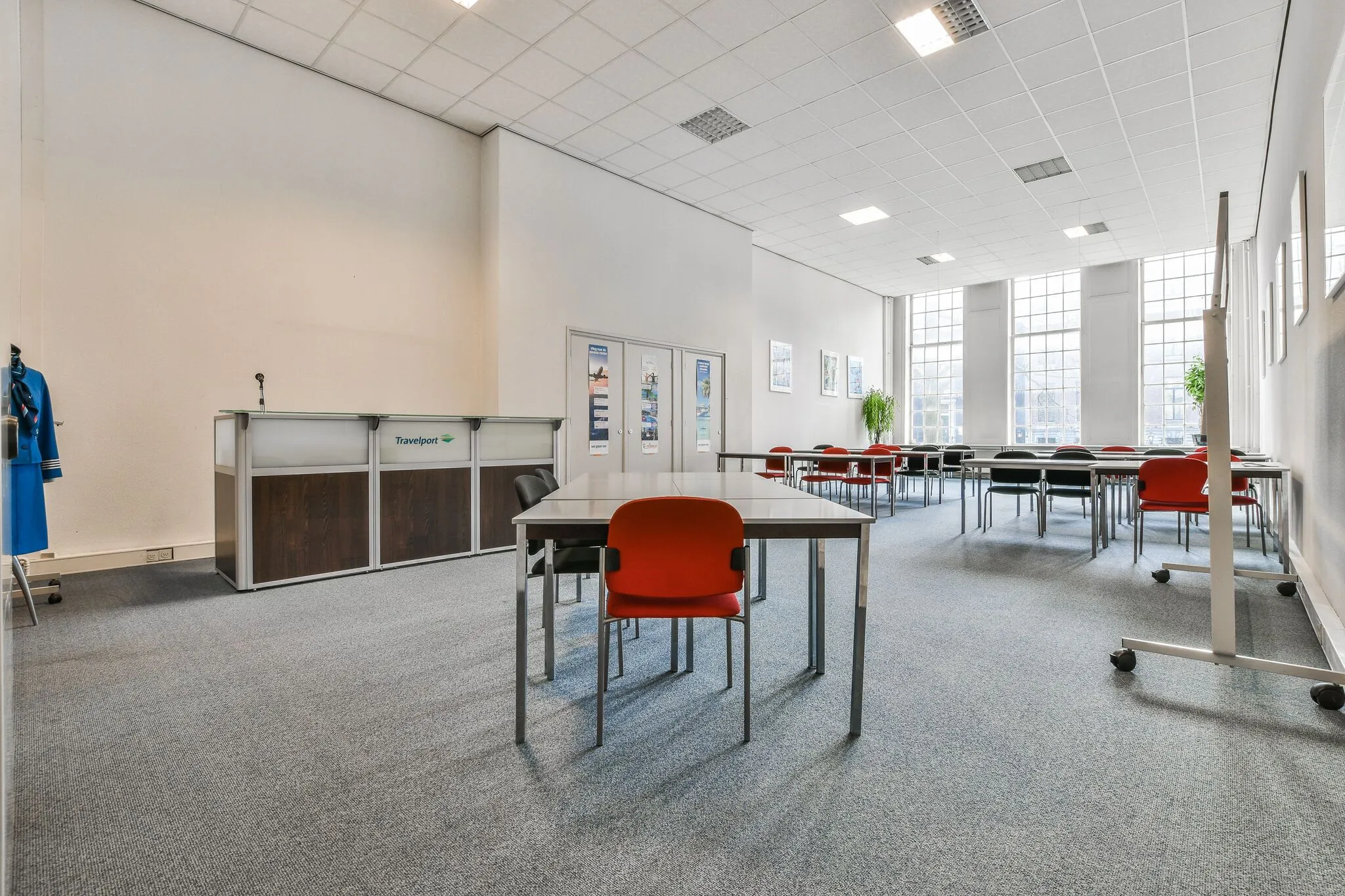 Ruime vergaderruimte aan de Herengracht met grote ramen, tafels, stoelen en een balie met het logo van Travelport.