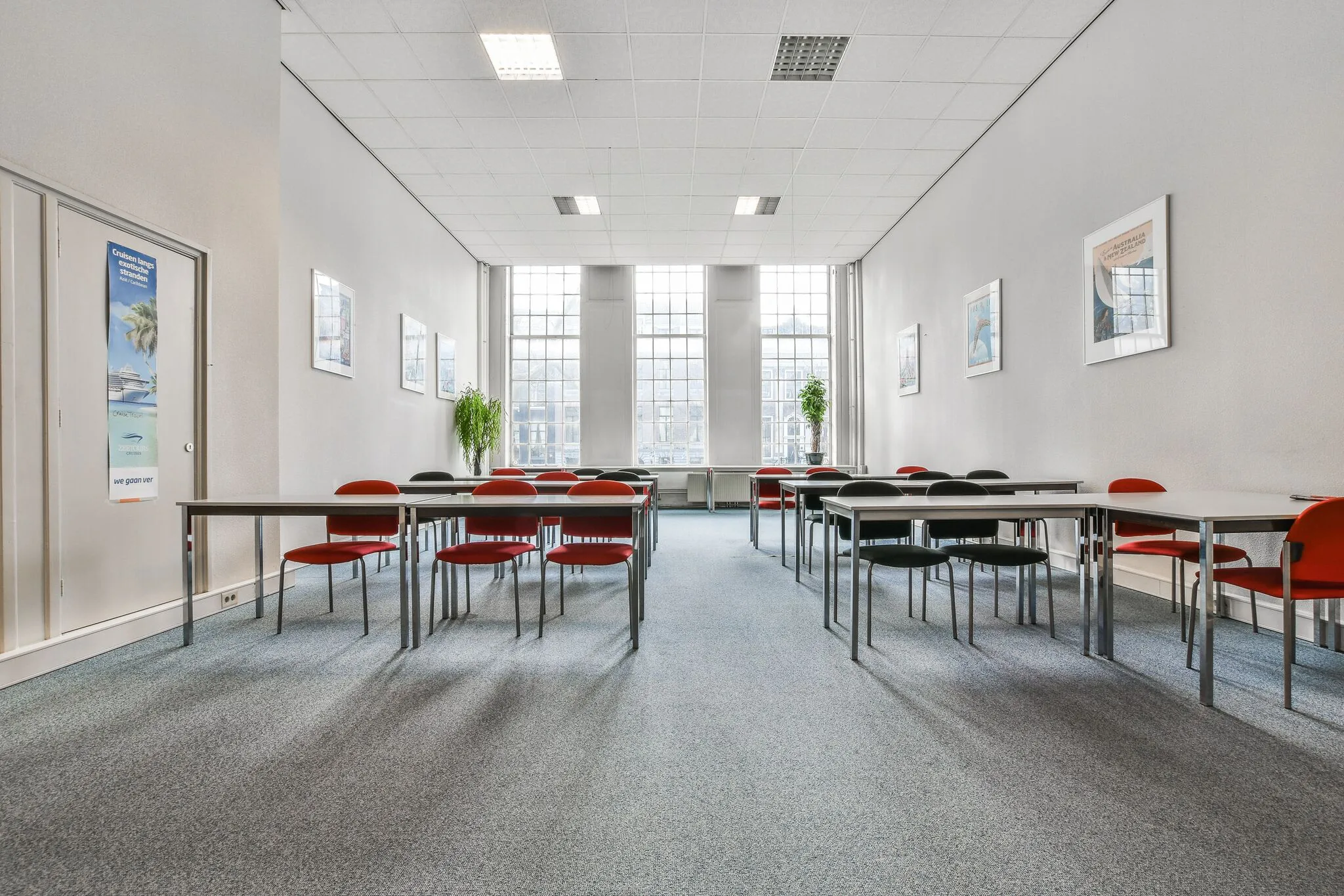 Vergaderruimte aan de Herengracht met opgestelde tafels, rood-zwarte stoelen en grote ramen die veel daglicht binnenlaten.