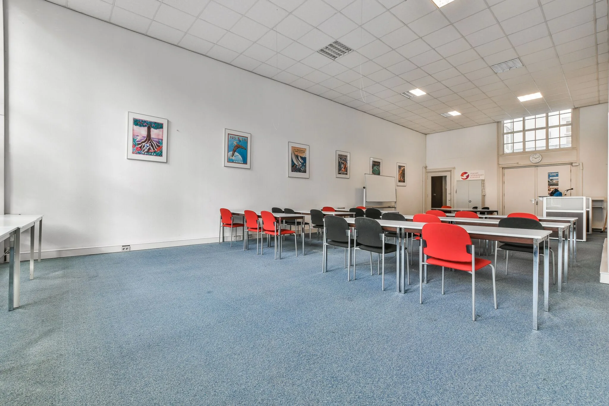 Vergaderzaal aan de Herengracht met rijen tafels en rood-zwarte stoelen, kunst aan de muur en een spreekgestoelte voorin.