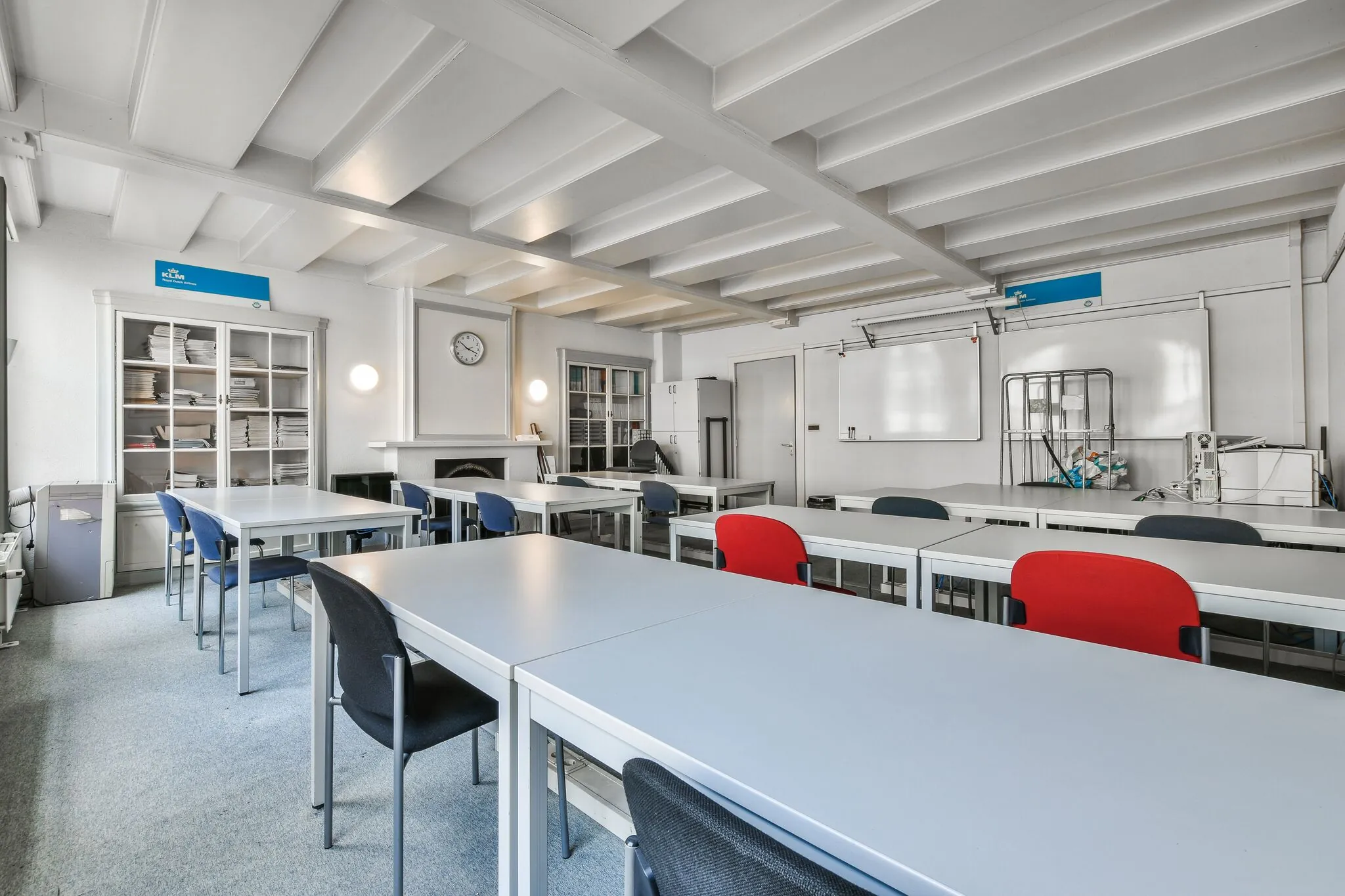 Licht klaslokaal aan de Herengracht met witte tafels, gekleurde stoelen en een whiteboard aan de muur.