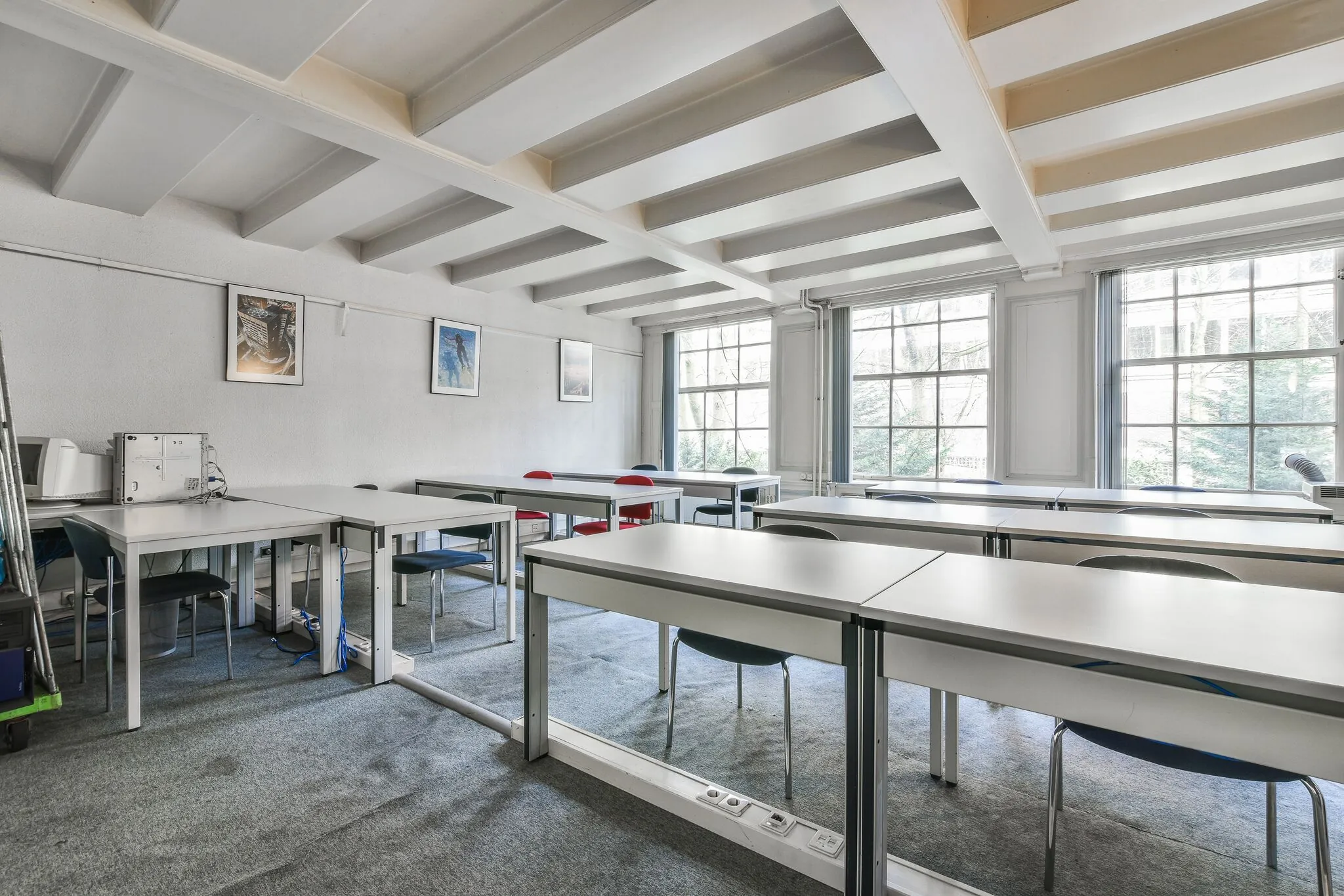 Licht klaslokaal aan de Herengracht met moderne bureaus, stoelen en grote ramen.