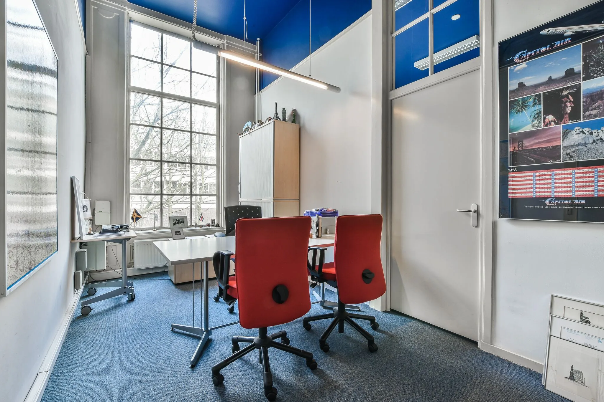 Modern kantoor met hoge ramen, twee rode bureaustoelen en een speelse inrichting aan de Herengracht.