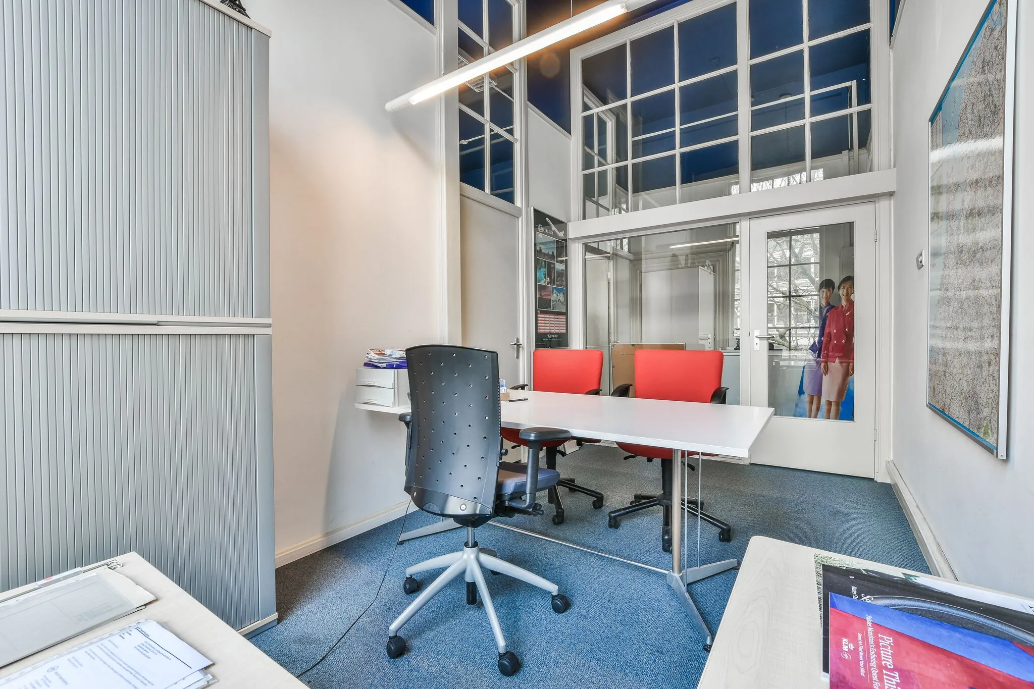 Kleine vergaderruimte met witte muren, rode stoelen en grote ramen aan de Herengracht.