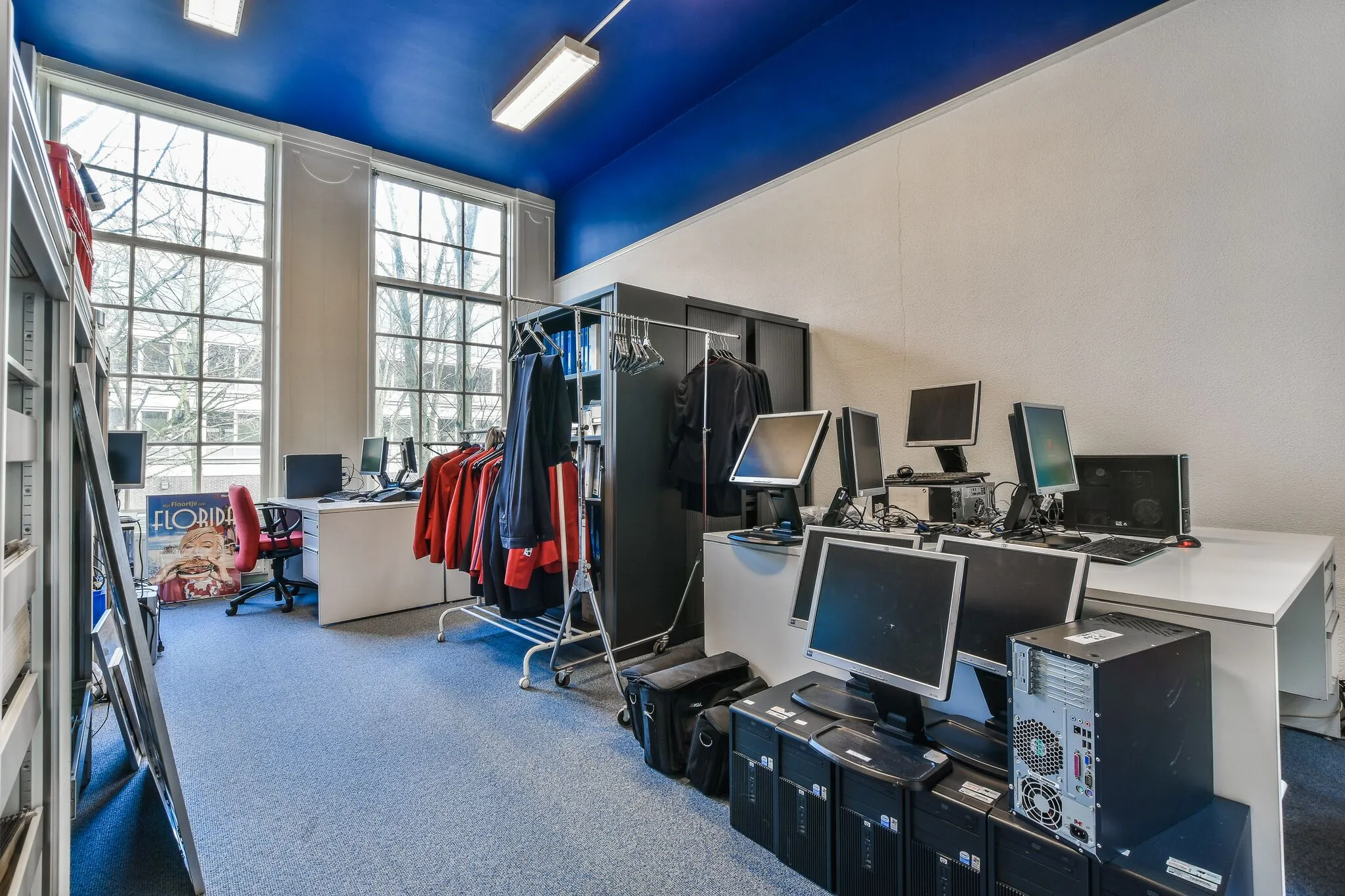 Kantoorruimte aan de Herengracht met werkplekken, computers, kledingrekken en grote ramen met uitzicht op bomen.