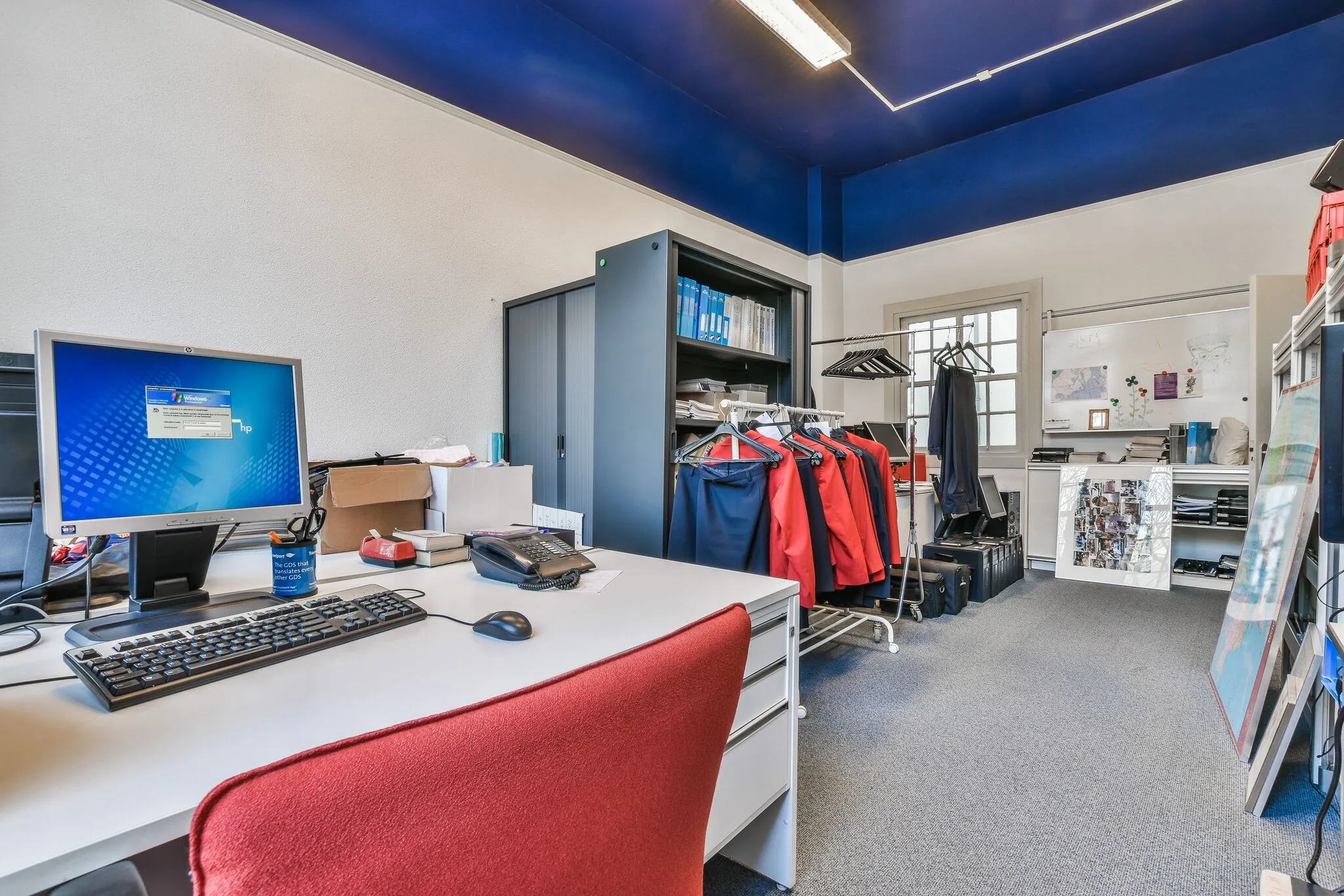 Kantoorkamer aan de Herengracht met bureau, kledingrekken met colberts en kasten vol kantoorbenodigdheden.