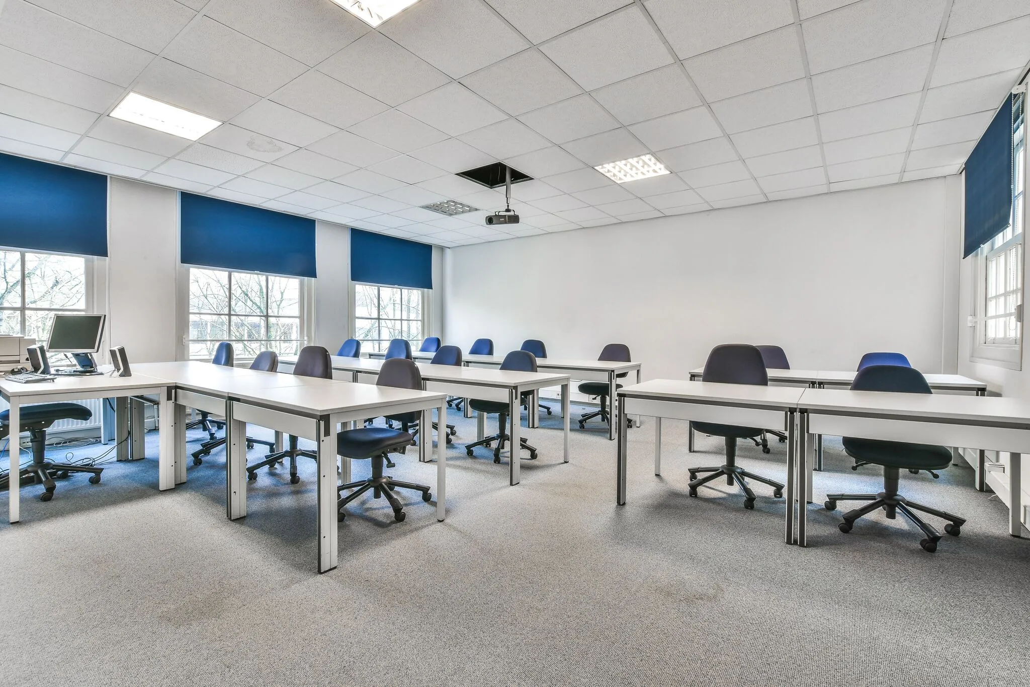 Licht en modern leslokaal aan de Herengracht met meerdere bureaus, bureaustoelen en een computeropstelling.