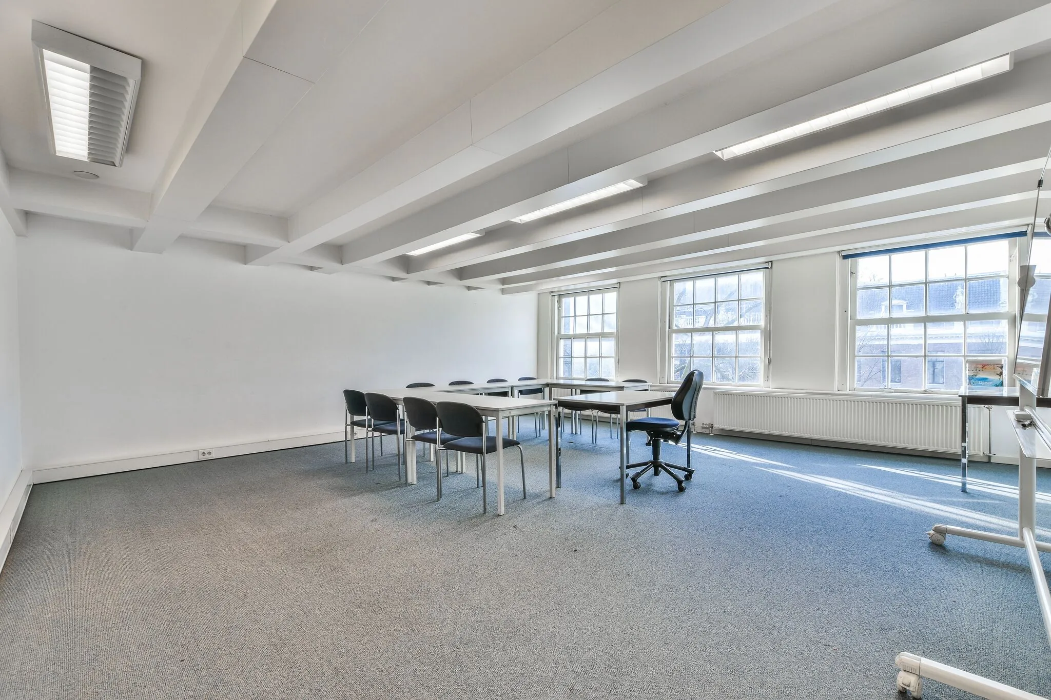 Licht en ruim vergader- of leslokaal aan de Herengracht met tafels, stoelen en grote ramen.