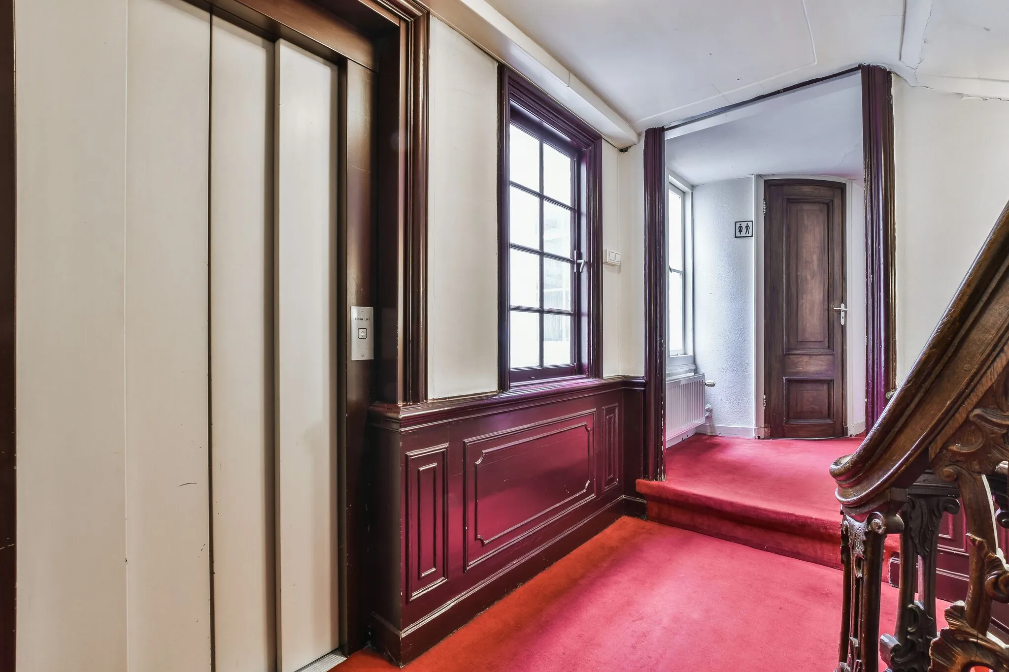 Hal met rode vloerbedekking in een historisch pand aan de Herengracht, met liftdeur, houten trapleuning en toiletruimte.