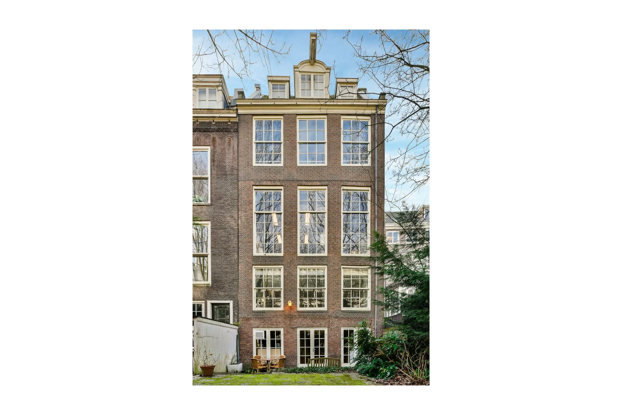 Achtergevel van een klassiek herenhuis aan de Herengracht met grote ramen en een tuin met zitje.