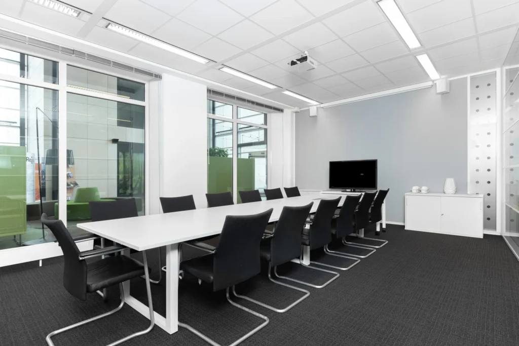 Moderne vergaderruimte met een lange tafel, zwarte stoelen en een scherm aan de muur.