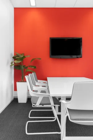 Een vergaderruimte met een fel oranje muur, moderne witte stoelen en een plantenbak.