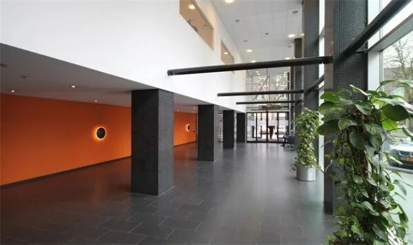 Moderne entreehal van een kantoorgebouw aan de Benthemstraat met zwarte zuilen, oranje accentmuur en grote ramen.